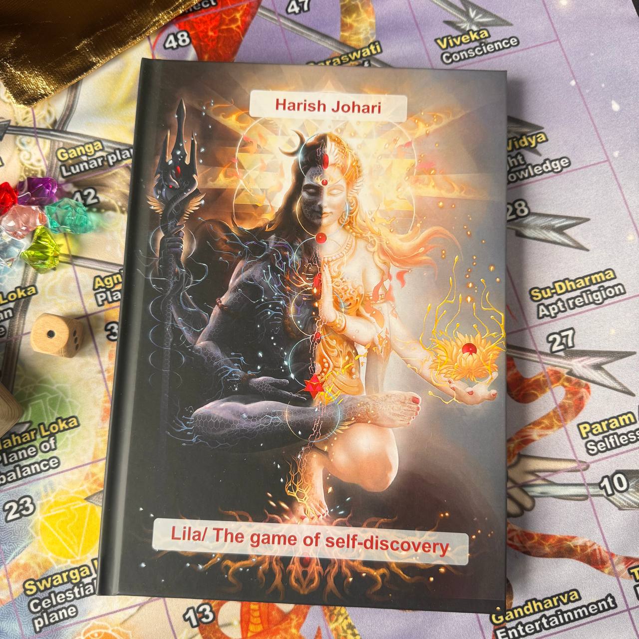 a book cover with an artistic depiction of a dual-headed deity, surrounded by flames and other mystical elements. The book cover is titled "Lila/The game of self-discovery" and is placed on a game board with various game pieces scattered around it.