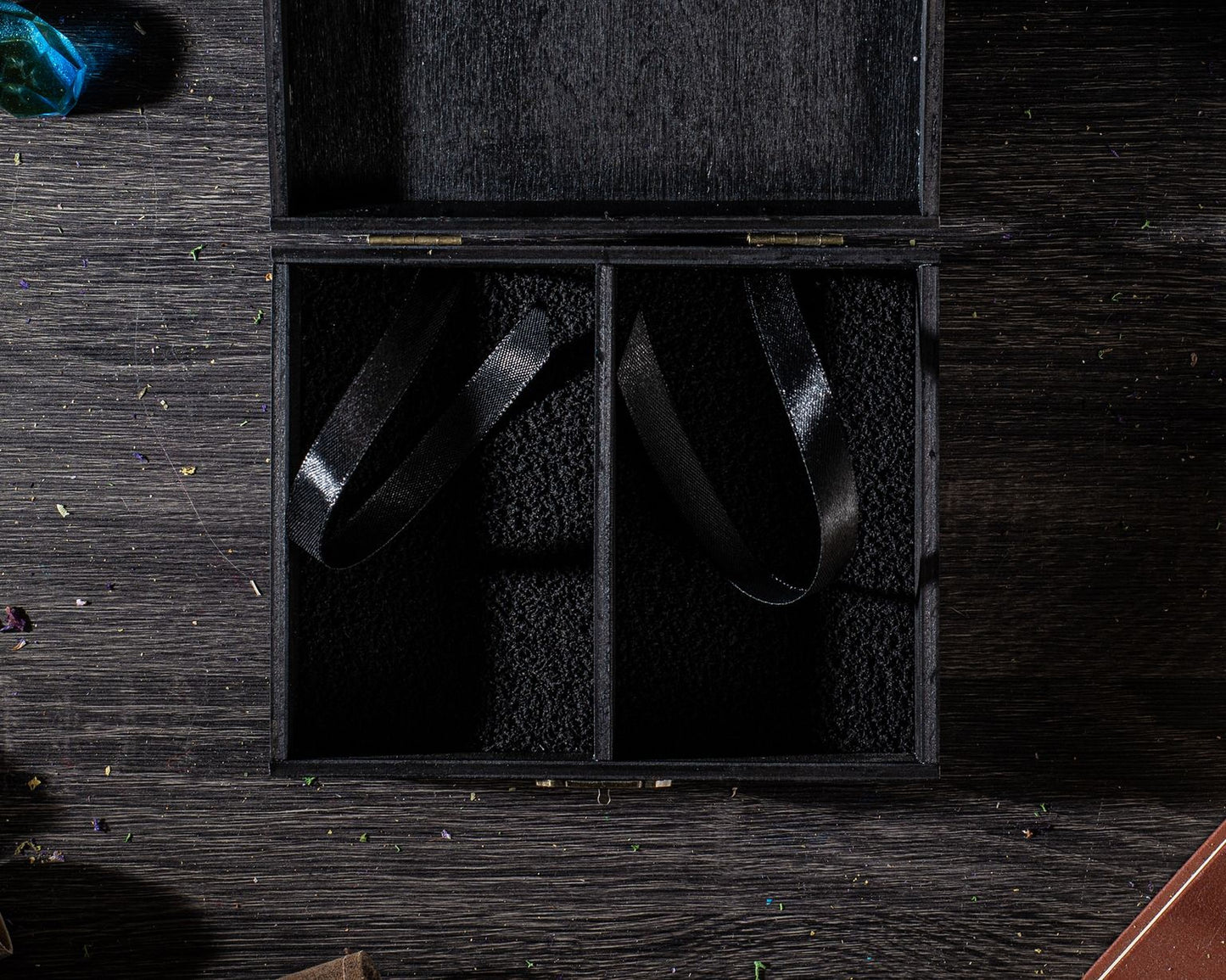 An open wooden box with two black straps inside, placed on a wooden surface.