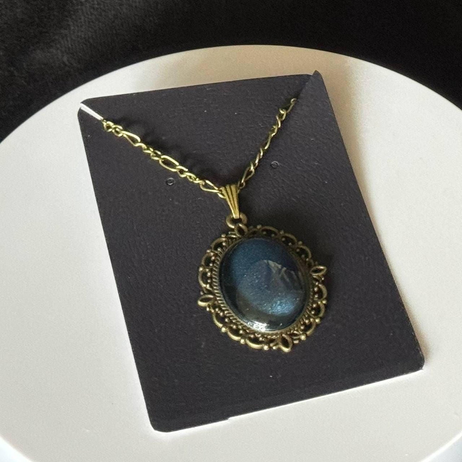 A necklace with a blue stone pendant is displayed on a black card.