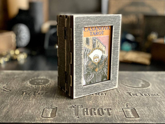 A wooden box with a tarot card inside, placed on a wooden surface with various symbols and text related to tarot cards.