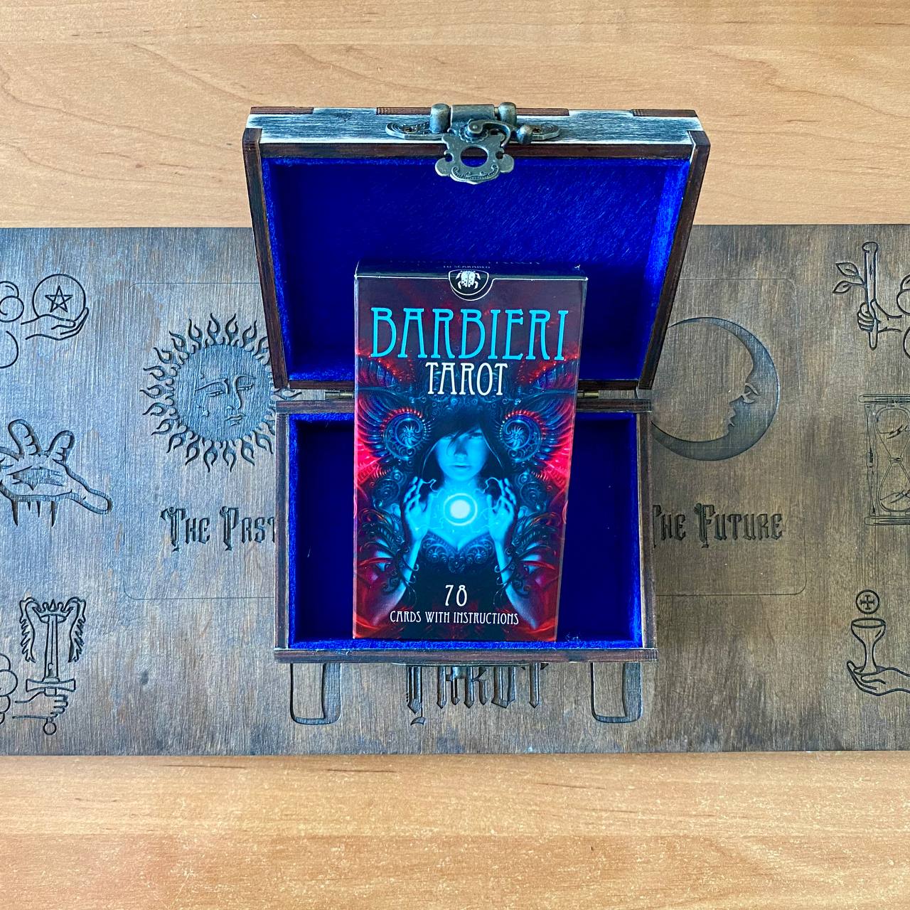 A wooden box containing a tarot deck with a blue interior, featuring a central image of a woman with a glowing orb on her chest.