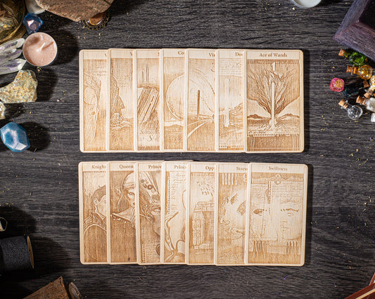 A collection of wooden tarot cards arranged on a dark wooden surface, with various objects such as gemstones, crystals, and other items scattered around them.