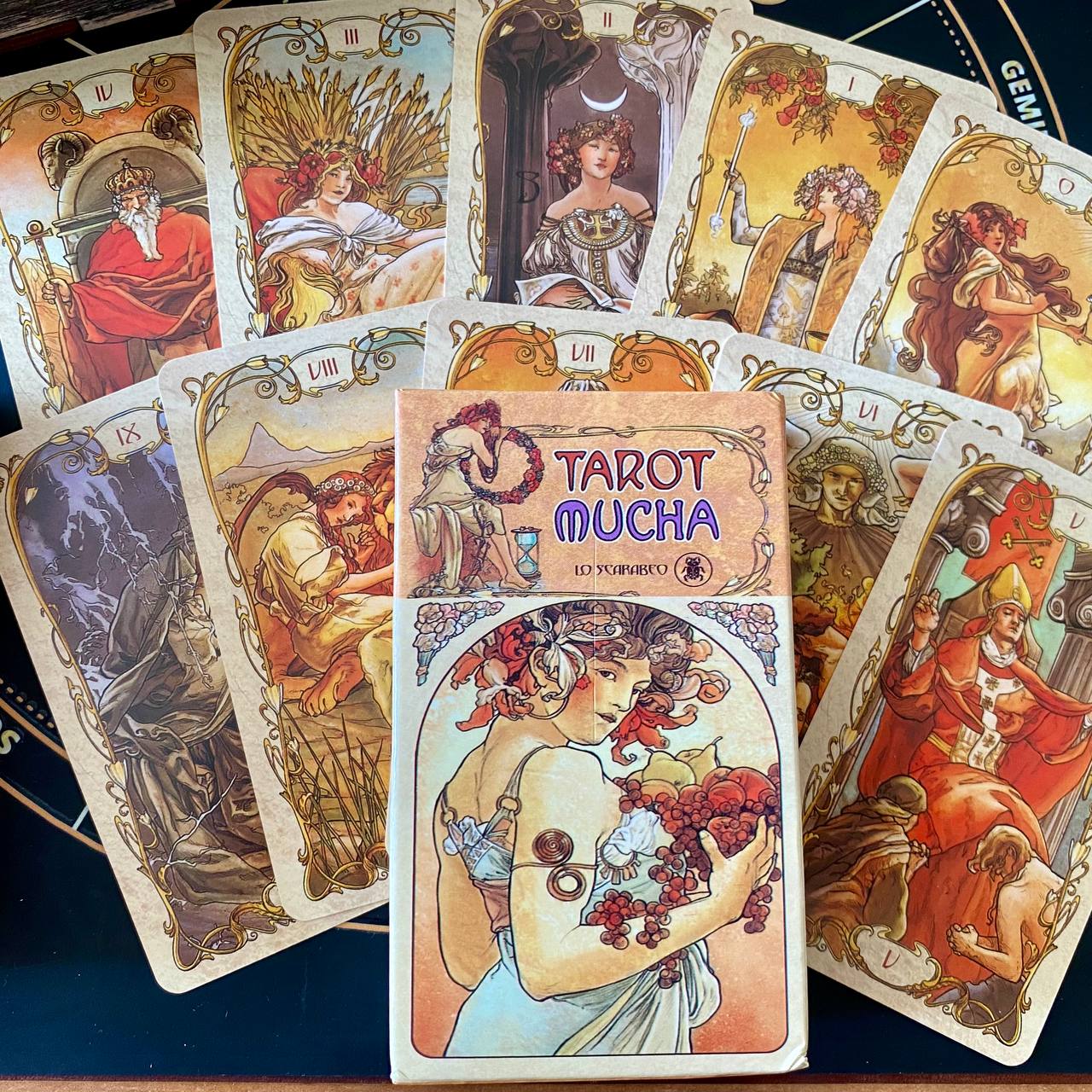a collection of tarot cards with intricate artwork and ornate designs, including a book titled "Tarot Mucha" in the foreground.