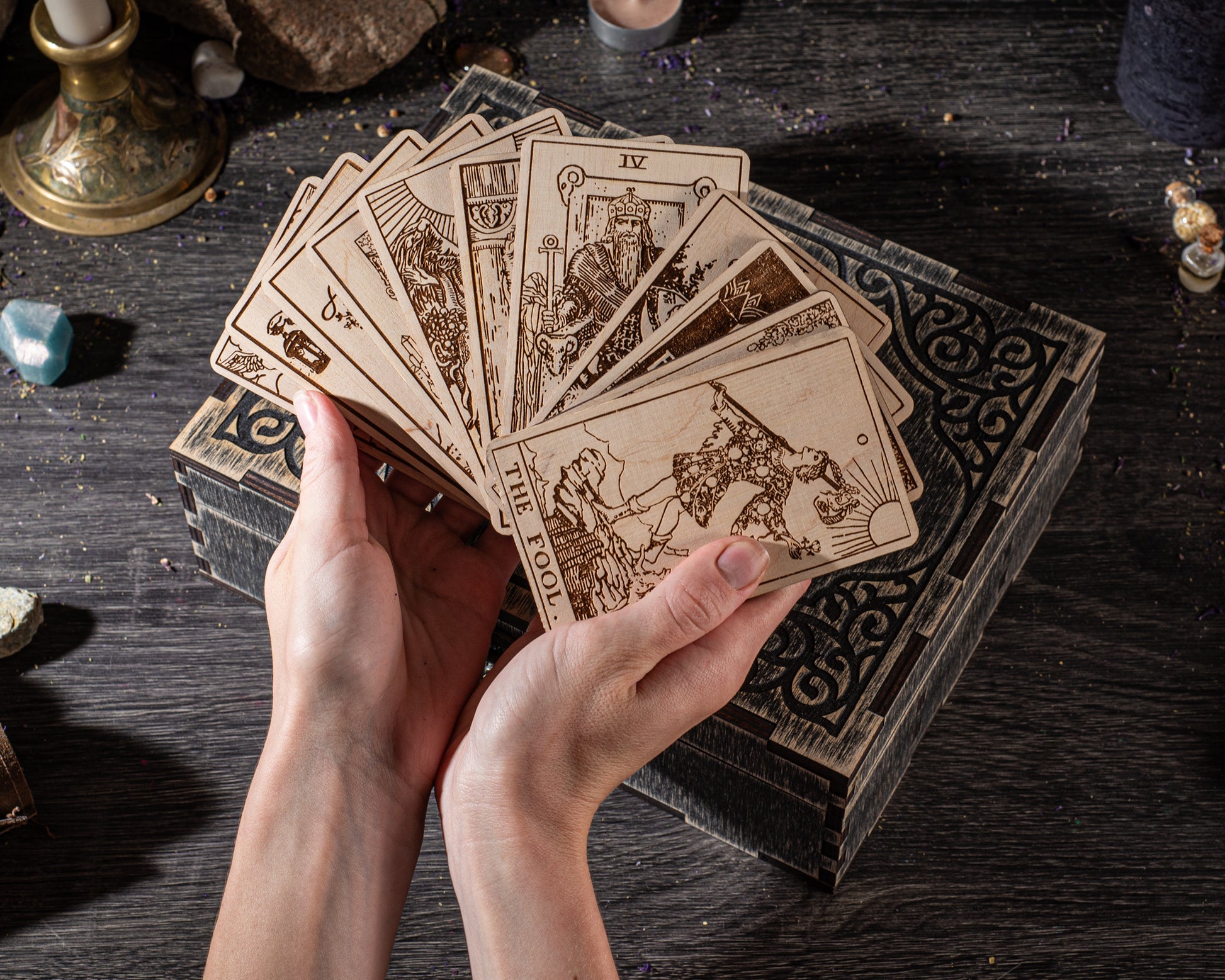 A pair of hands holding a deck of tarot cards, with the cards spread out on a wooden surface.