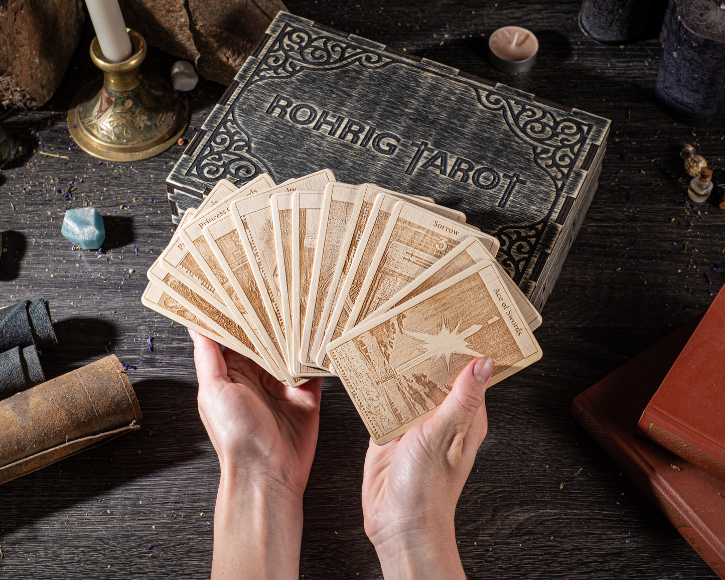 A pair of hands holding a deck of playing cards, with a tarot card box in the background.