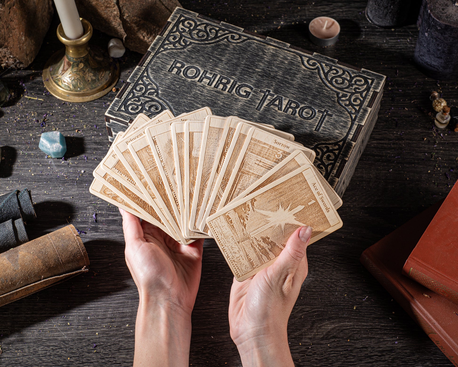 A pair of hands holding a deck of playing cards, with a tarot card box in the background.