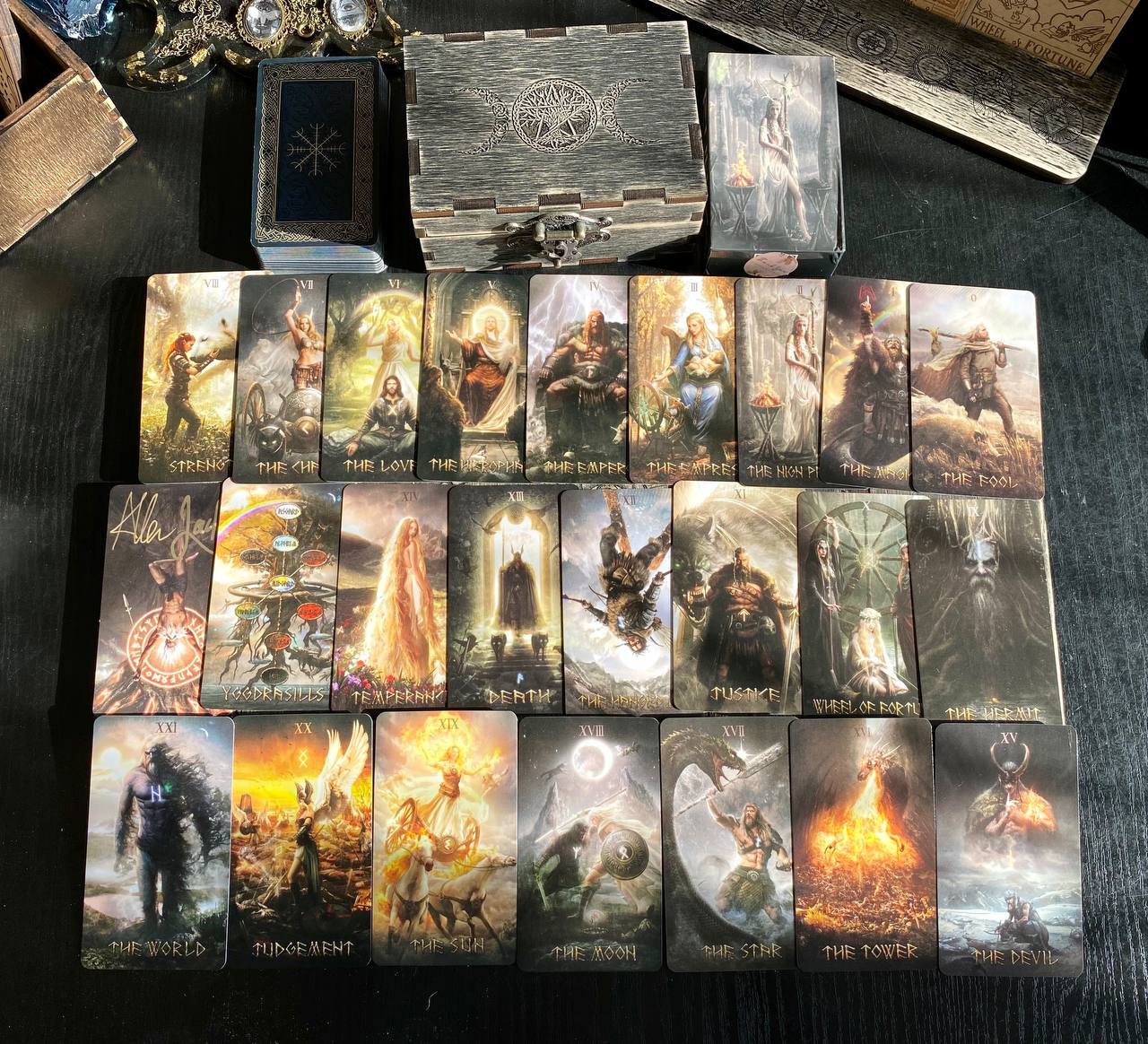 a collection of tarot cards arranged on a dark surface, with a wooden box and other items in the background.