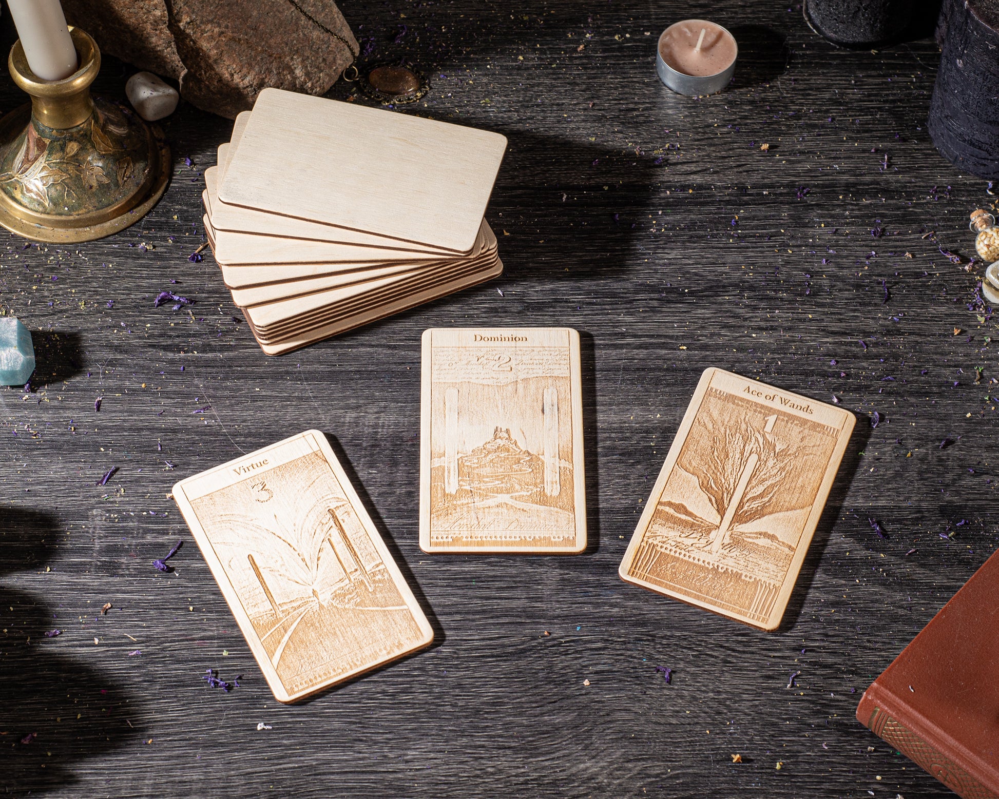 three wooden tarot cards with intricate designs, placed on a dark wooden surface. There are also various objects such as a candle, a book, and some crystals scattered around the cards.