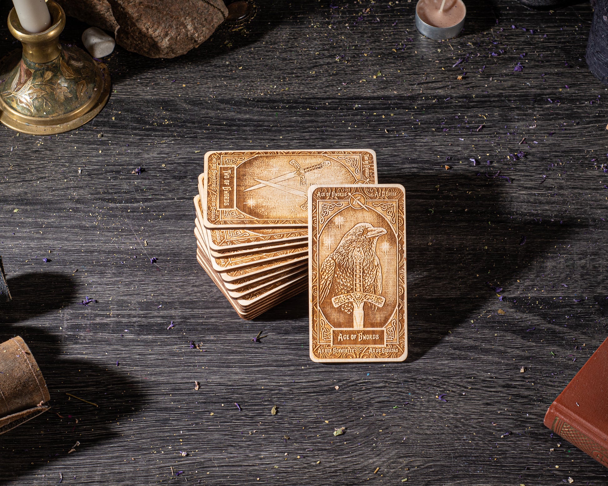 A stack of wooden cards with intricate designs, including a card with a bird and the text "Ace of Swords" on it, is placed on a dark wooden surface.
