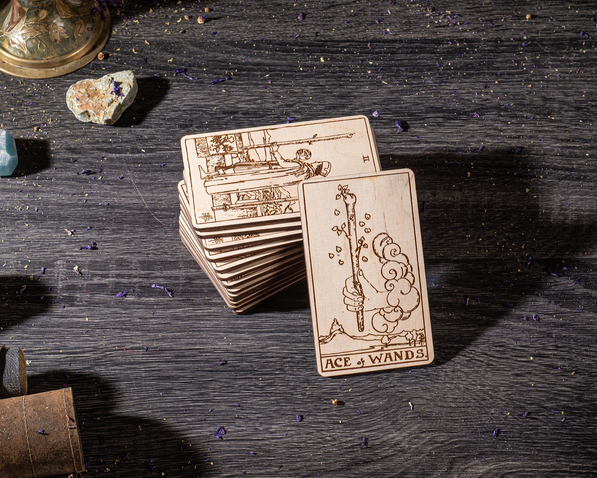 A stack of wooden cards with illustrations on them, placed on a wooden surface with scattered purple objects around.