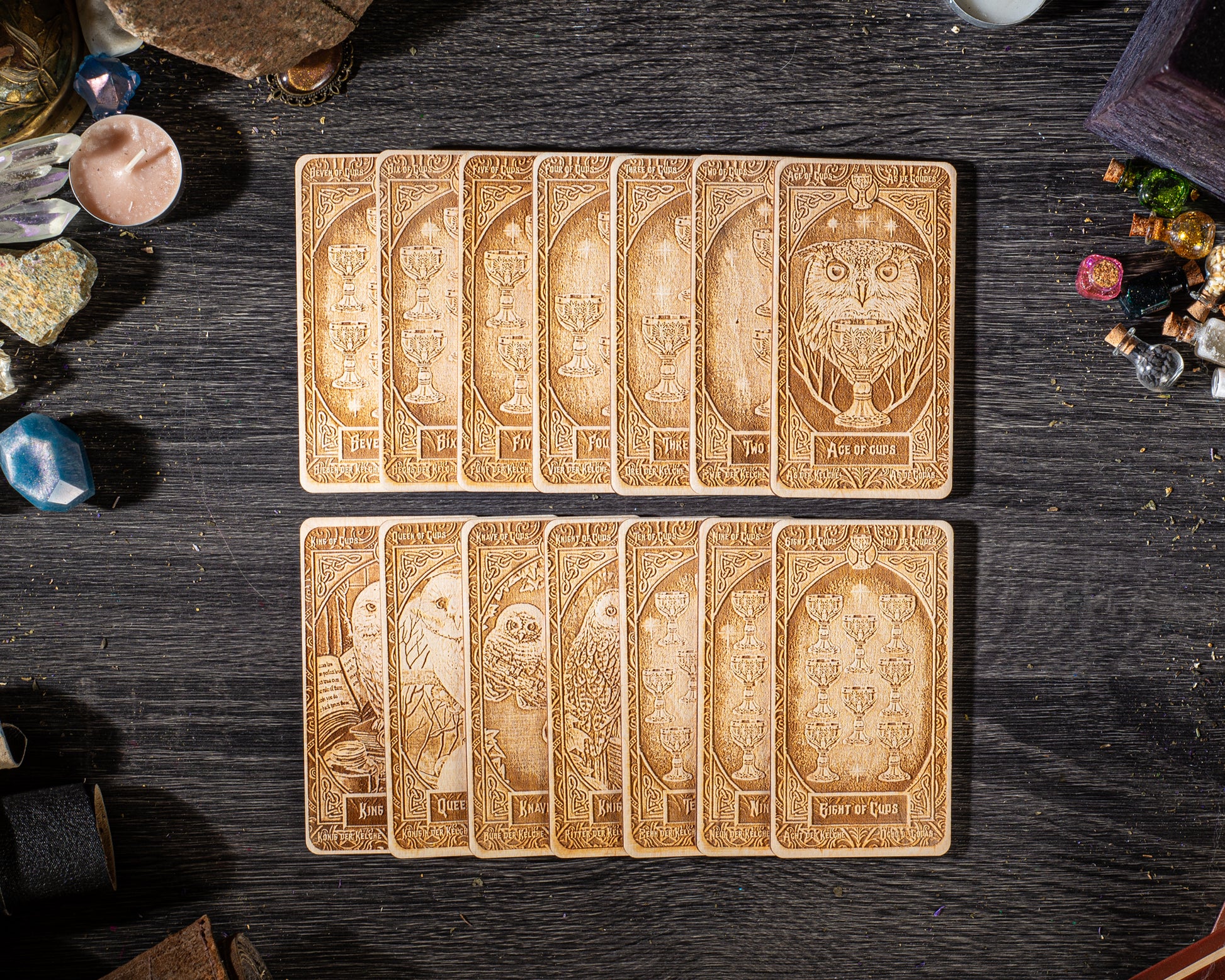 A collection of wooden tarot cards arranged on a dark wooden surface, with various objects such as gemstones and candles scattered around them.