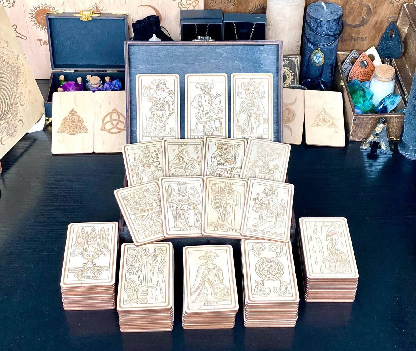 a collection of tarot cards arranged on a table, with various other items such as candles, crystals, and other objects in the background.