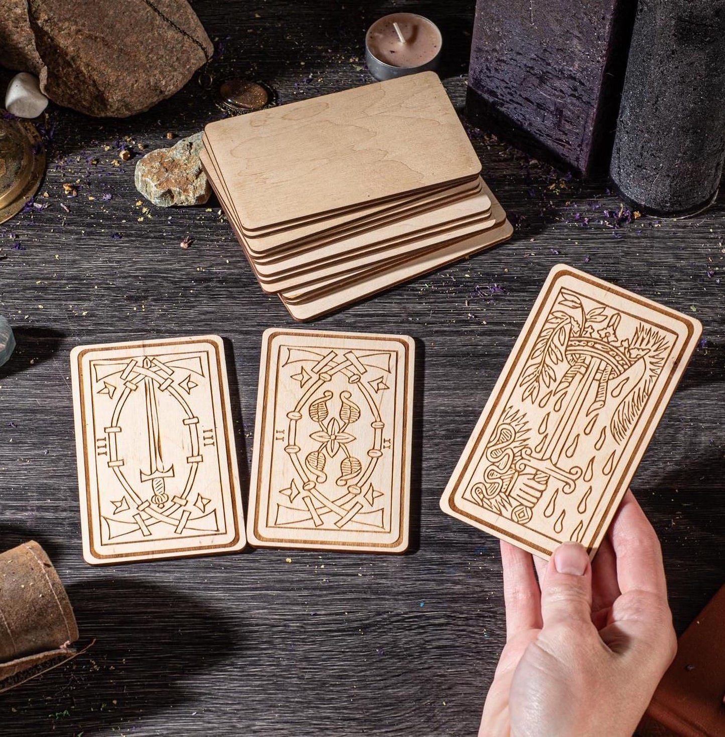 a hand holding three wooden tarot cards with intricate designs, arranged on a wooden surface.