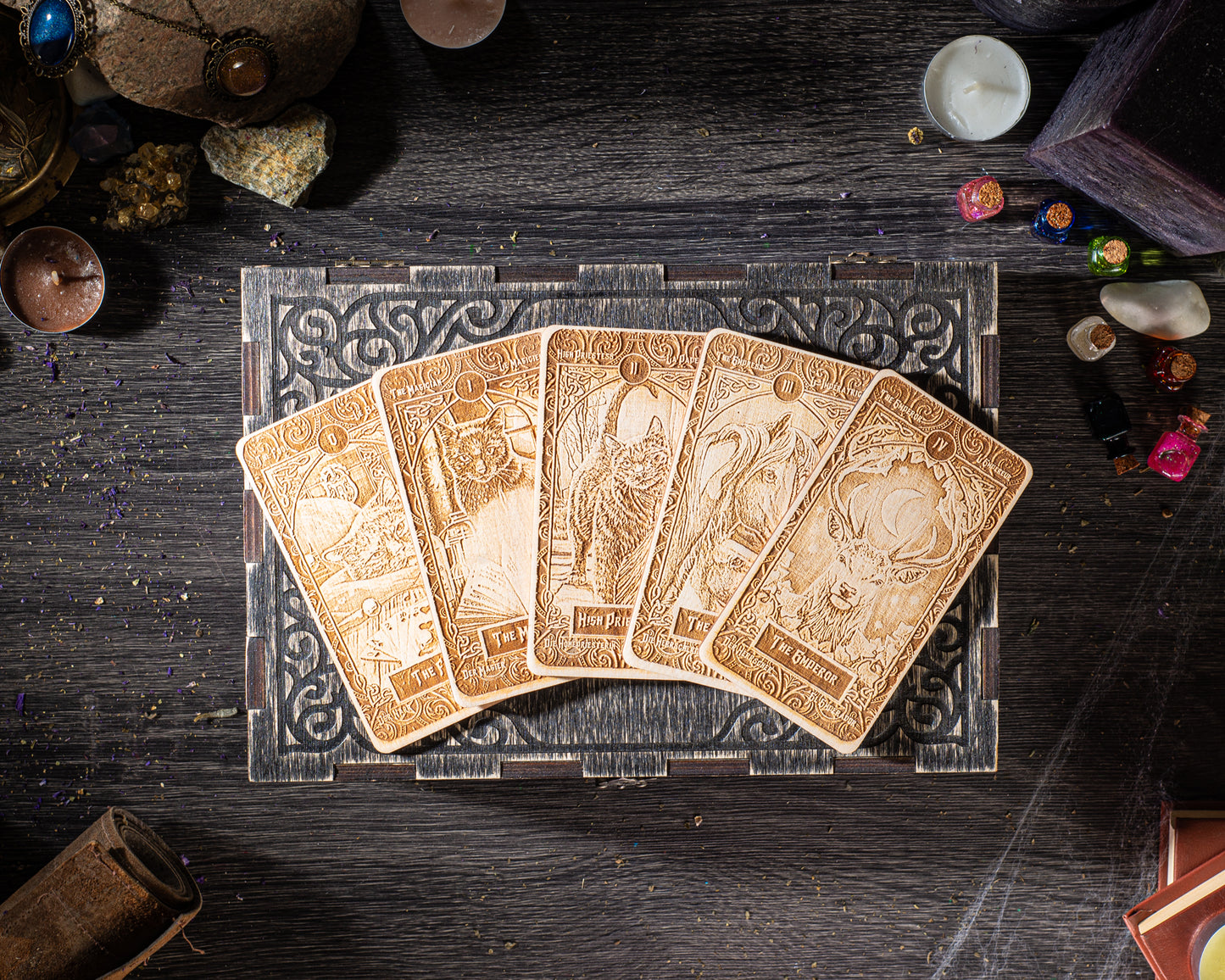 a collection of five ornate tarot cards arranged on a wooden surface, surrounded by various objects such as candles, gemstones, and other decorative items.