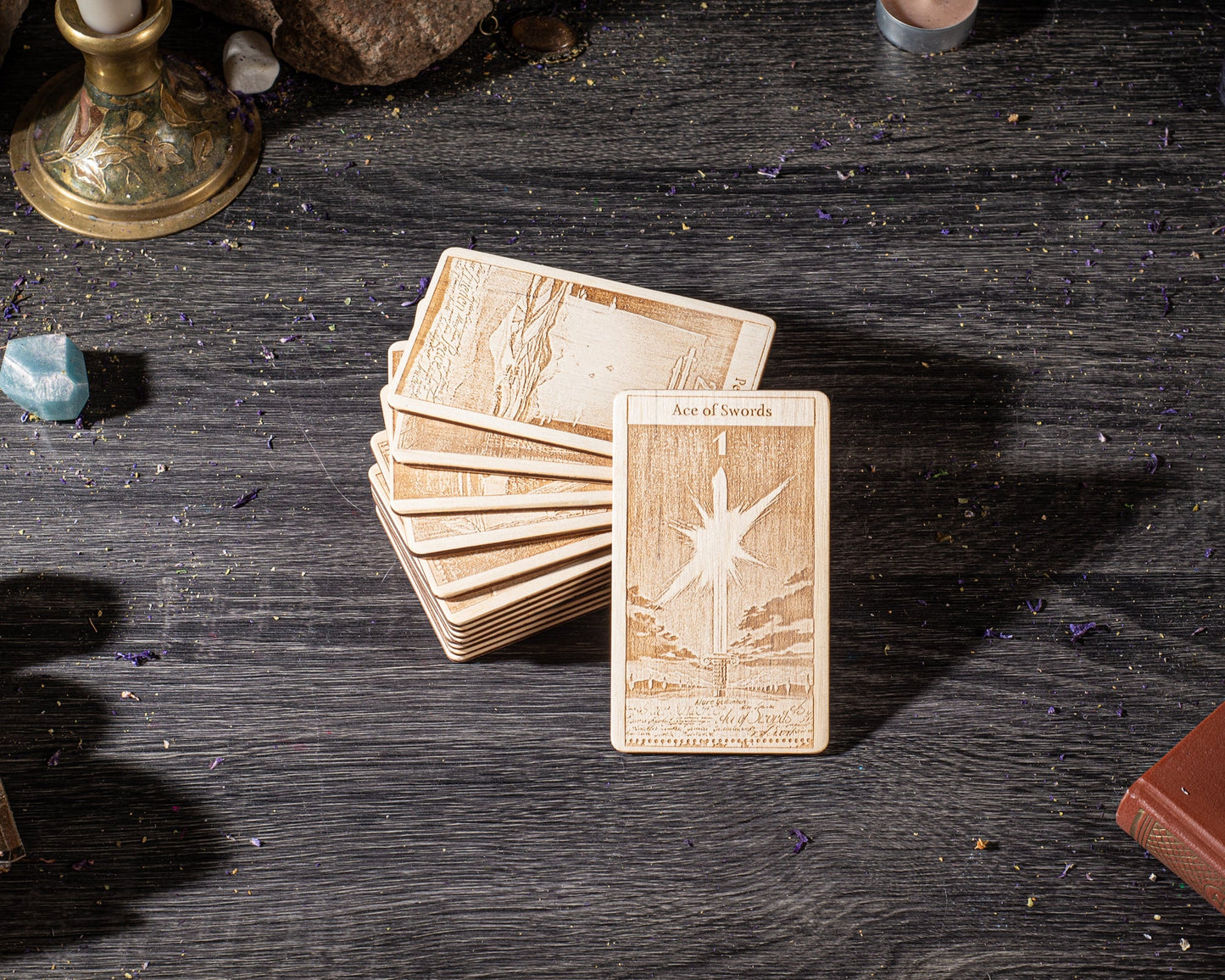 A stack of wooden cards with intricate designs, including a card with a star and the text "Ace of Swords" on it, is placed on a dark wooden surface.