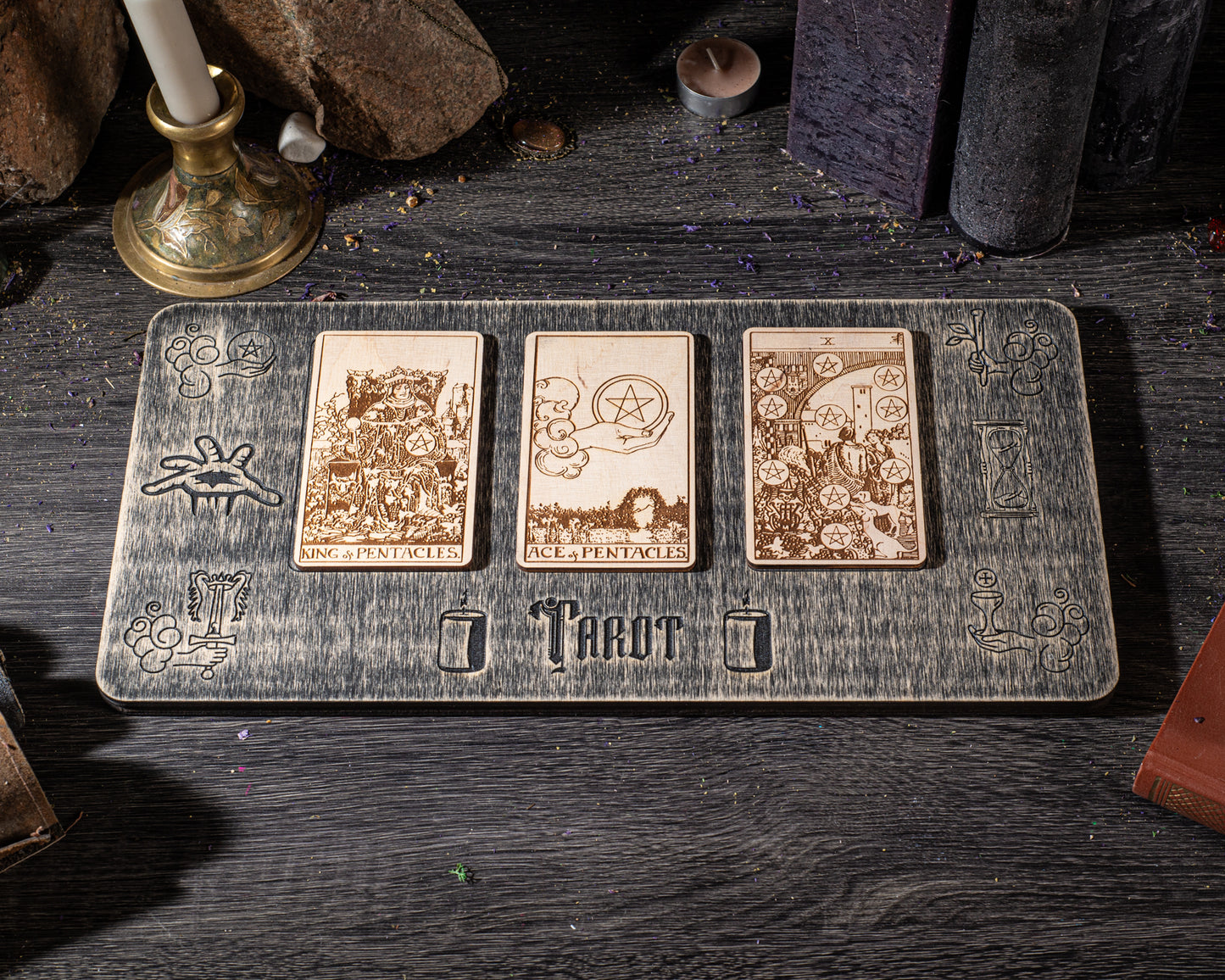 A wooden board with three tarot cards and the word "Trou" printed on it, placed on a wooden surface with candles and other objects in the background.