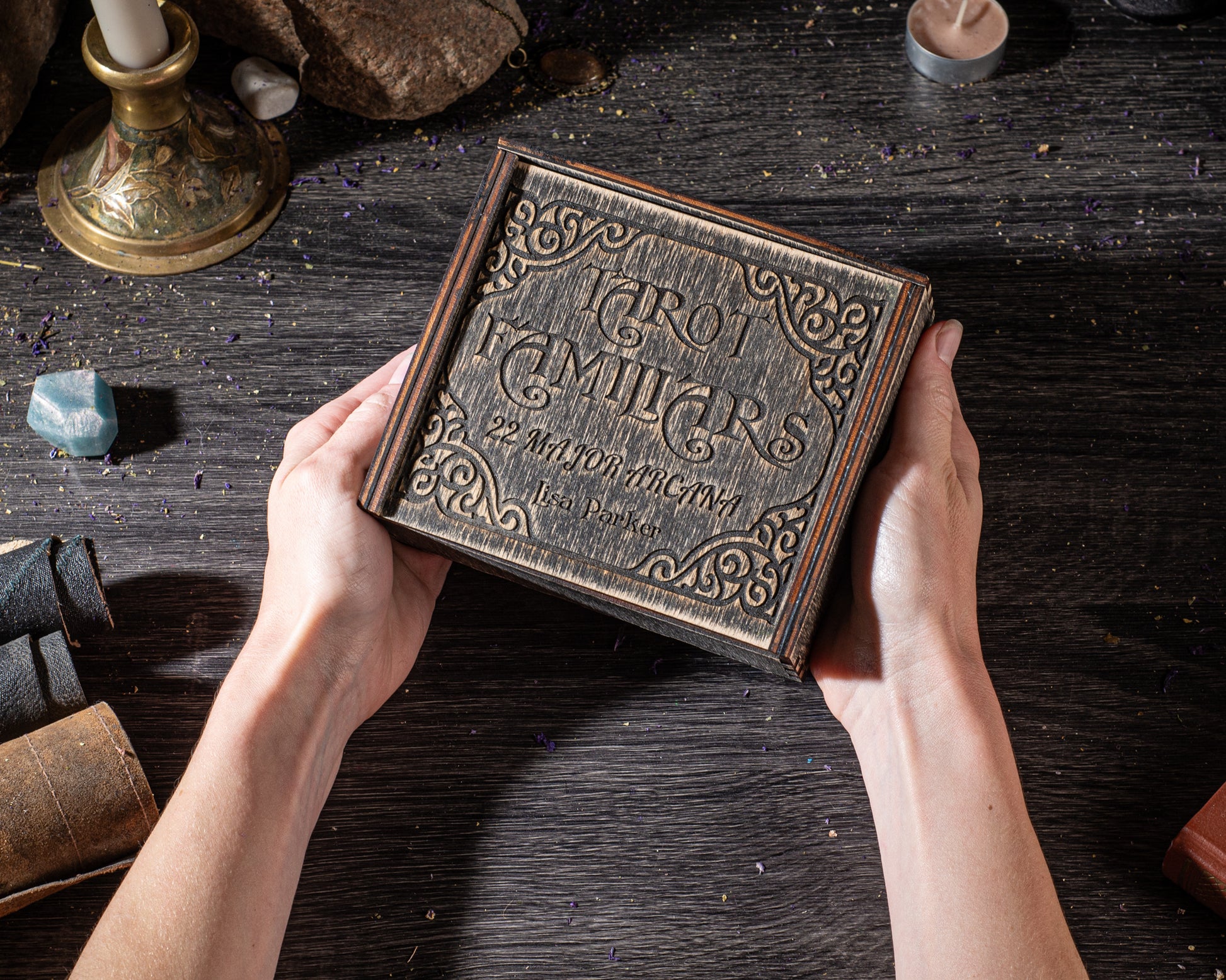 A person's hands holding a wooden box with an ornate design, placed on a dark wooden surface.