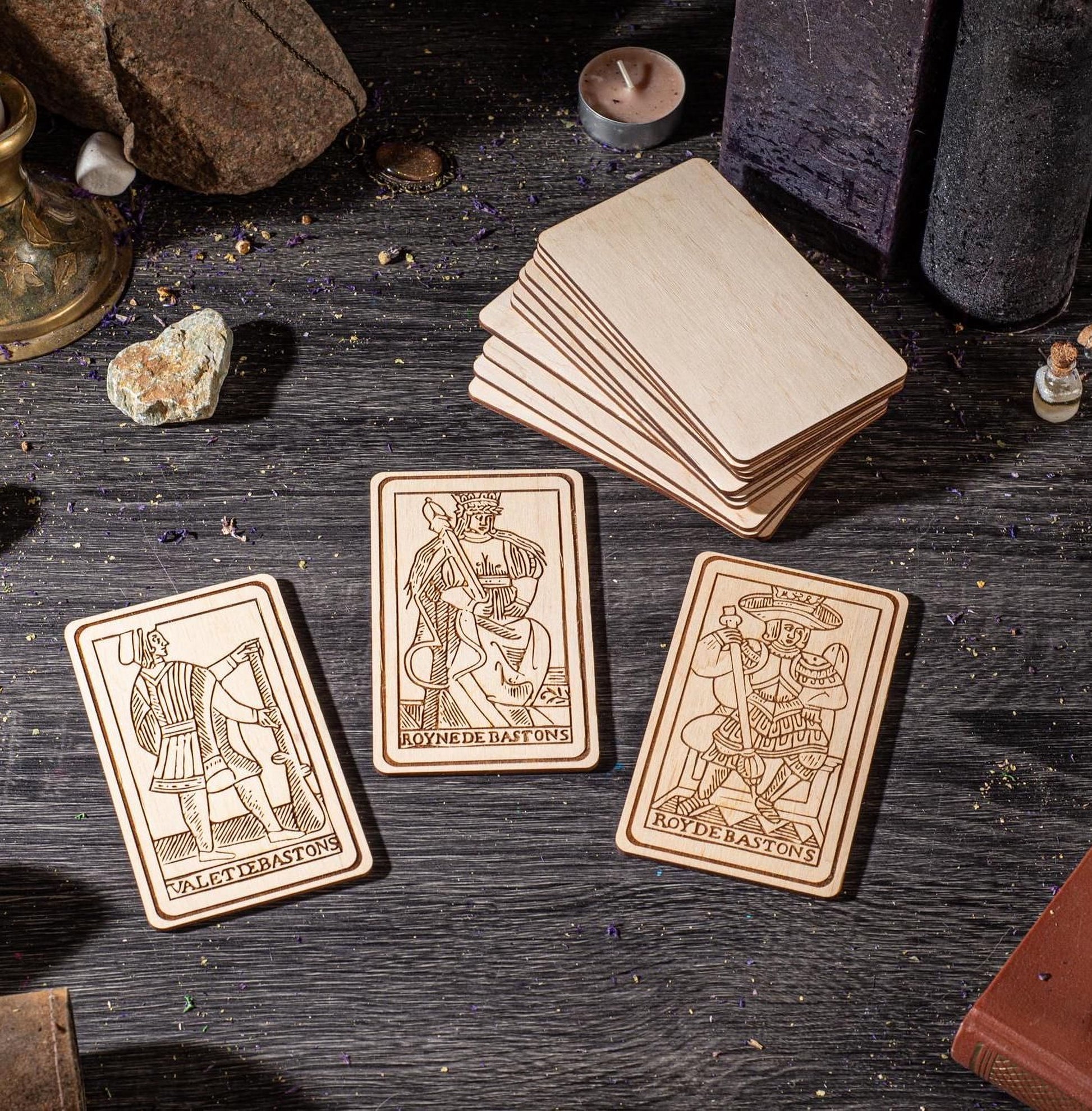 three wooden tarot cards with intricate designs, placed on a wooden surface alongside various objects such as candles, crystals, and a book.