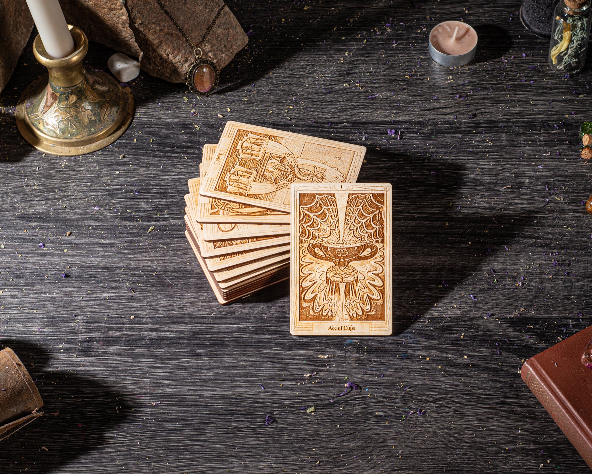 A stack of tarot cards is displayed on a dark wooden surface, surrounded by various objects such as a candle, a book, and a small figurine.