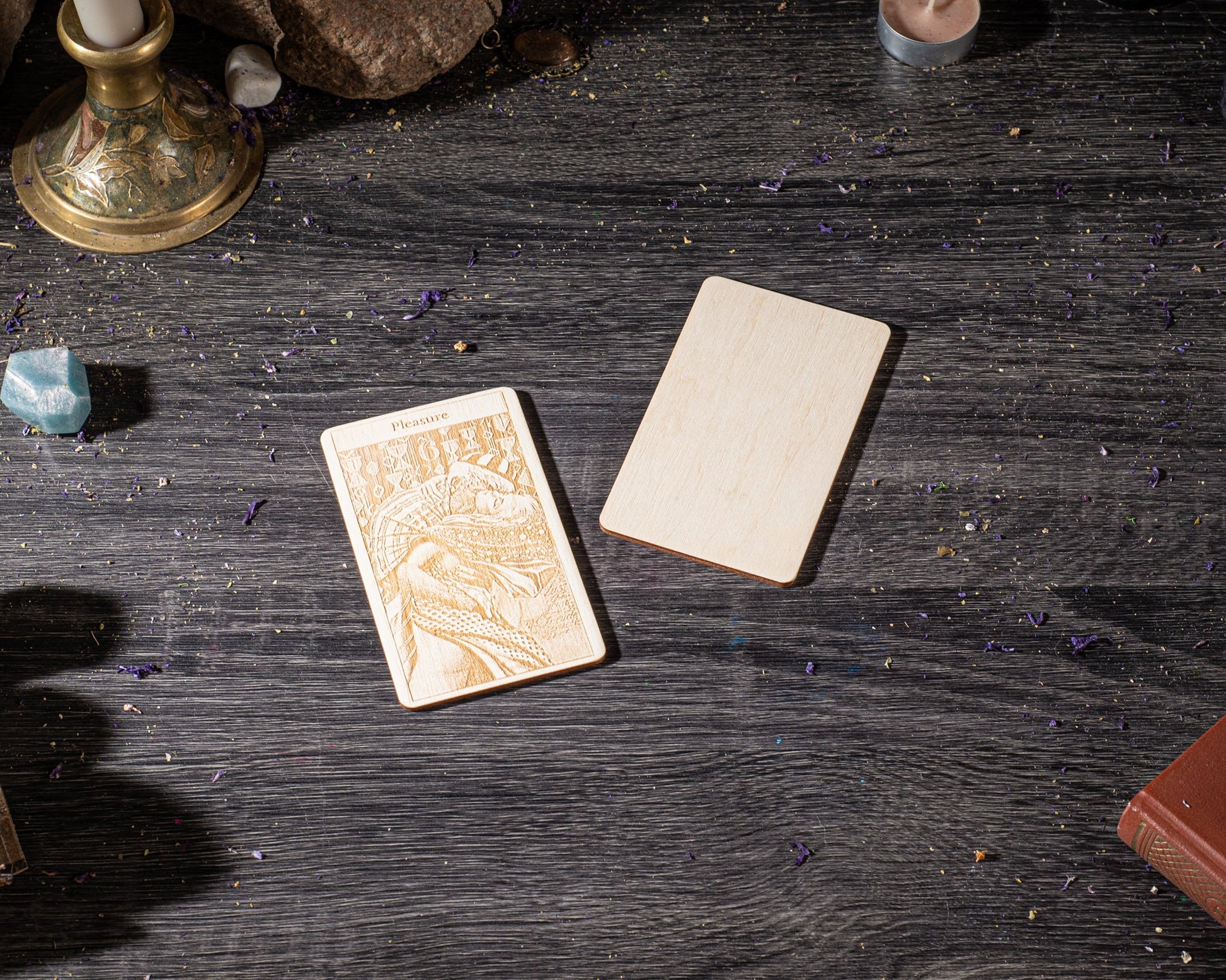 a wooden card with an embossed design, placed on a dark wooden surface alongside other objects such as a candle, a book, and some crystals.