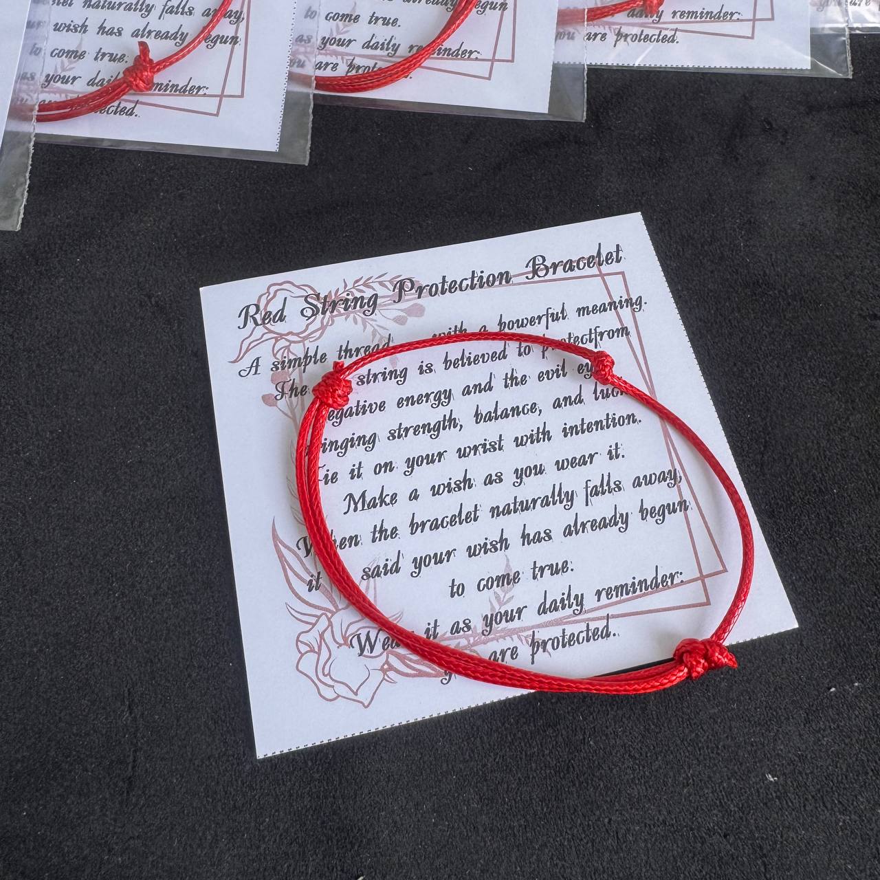 a red string bracelet with a white paper card displaying a red string bracelet prayer.