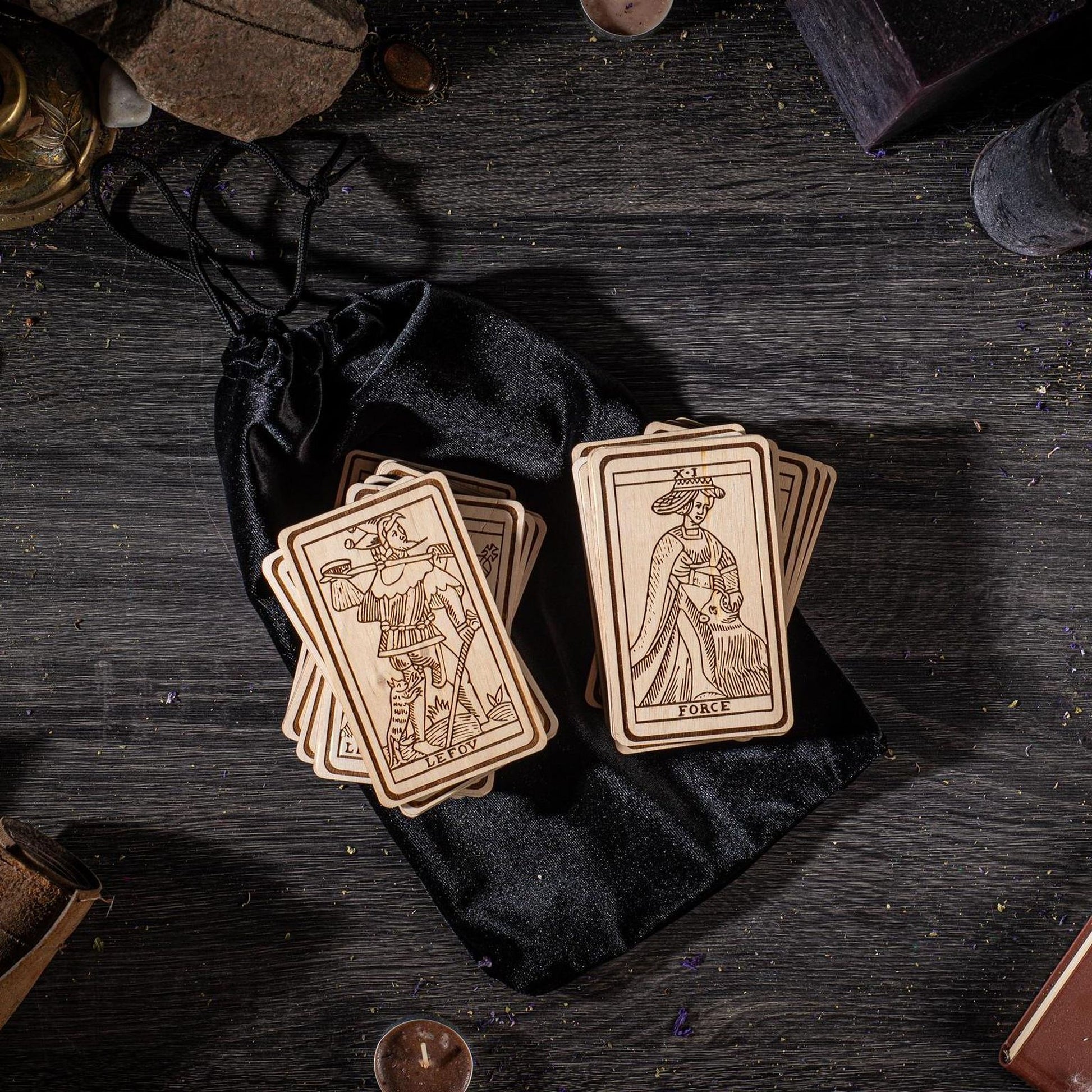a collection of wooden tarot cards placed on a black velvet bag, with various objects scattered around them on a wooden surface.