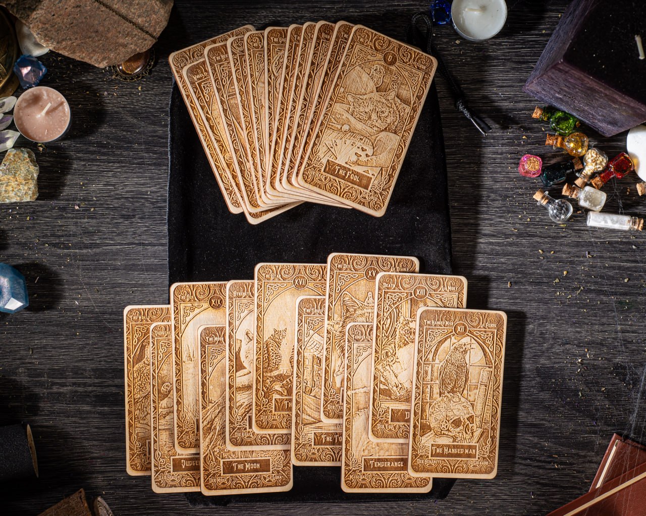 A collection of wooden tarot cards is spread out on a wooden surface, along with various other items such as candles, crystals, and small figurines.