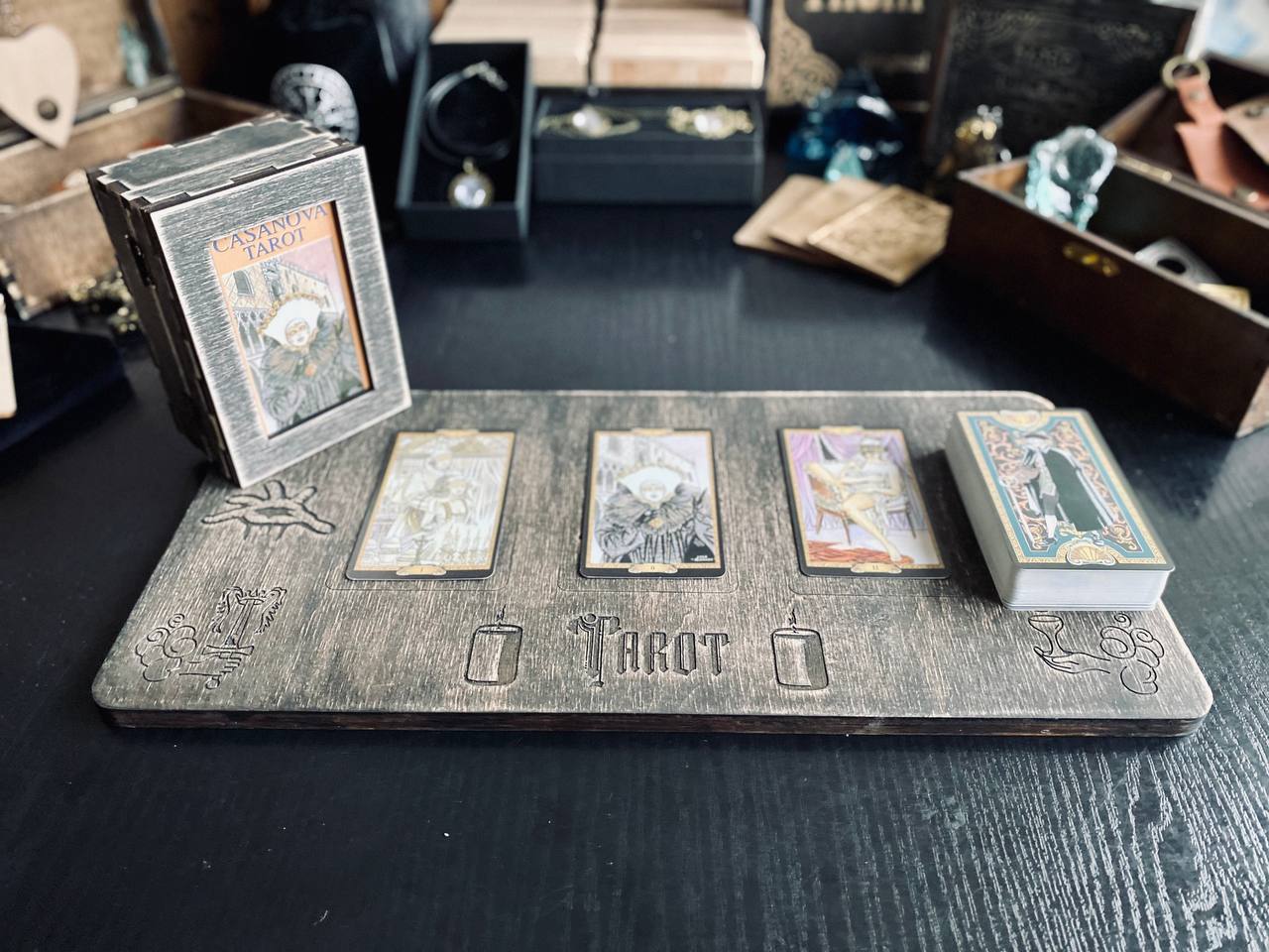 a wooden board with three tarot cards on it, along with a small wooden box and some other items on a table.