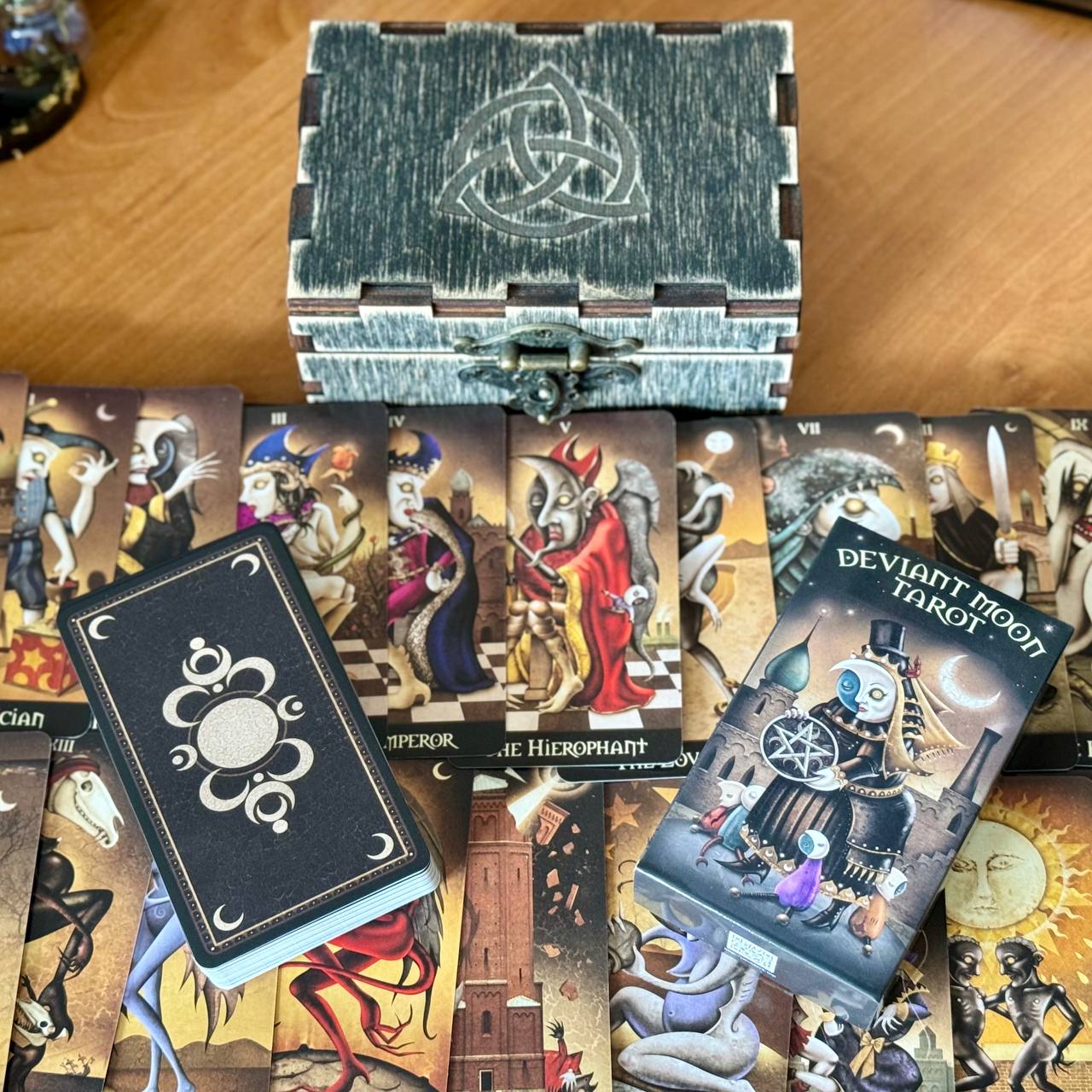 a collection of tarot cards and a wooden box with a Celtic knot design, arranged on a wooden surface.
