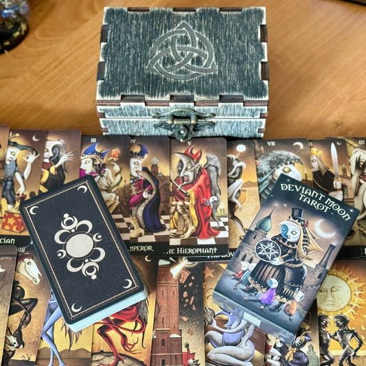 a collection of tarot cards and a wooden box with a Celtic knot design, arranged on a wooden surface.