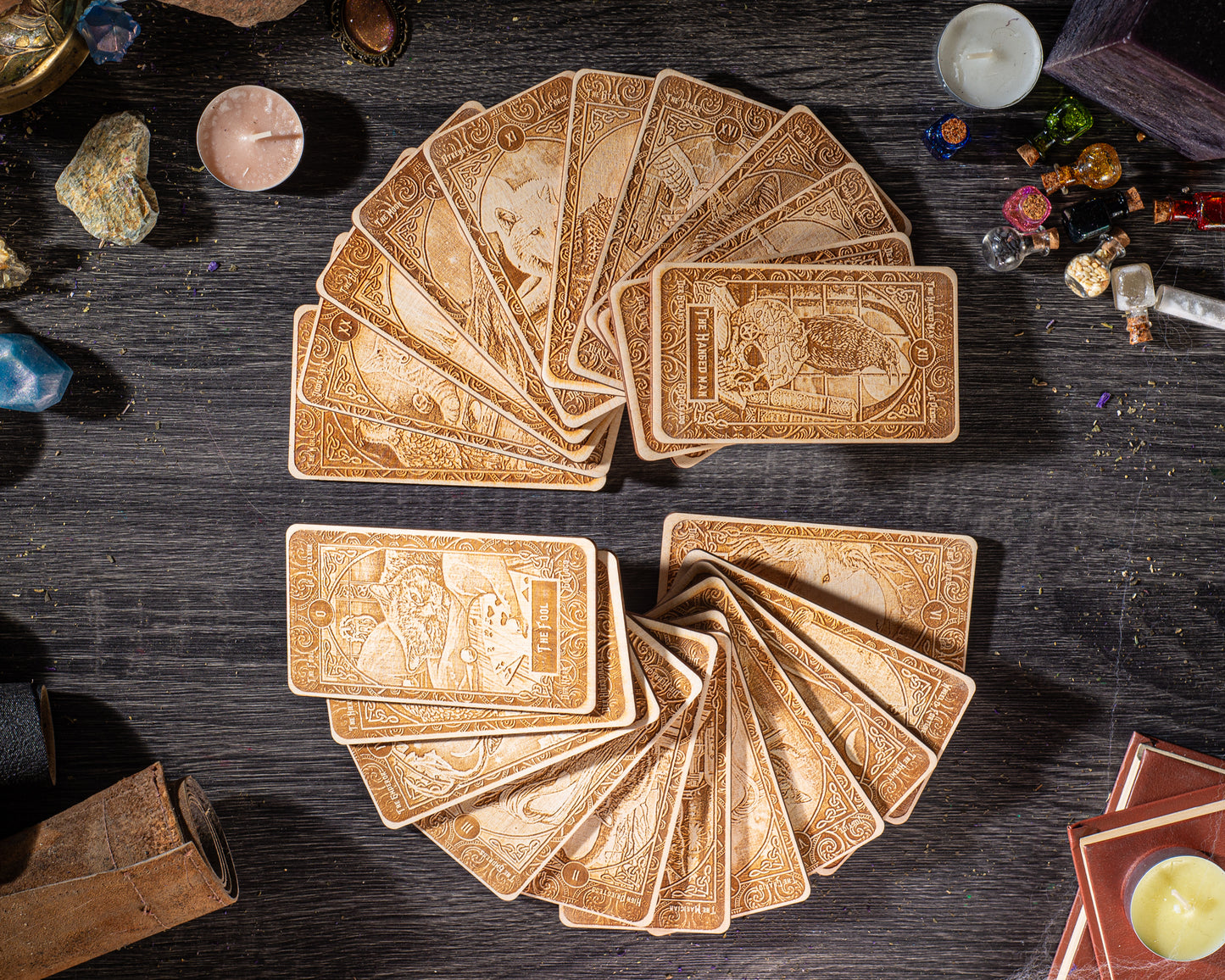 a collection of ornate wooden cards arranged in a circular pattern on a dark wooden surface, surrounded by various objects such as candles, gemstones, and books.