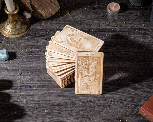 A stack of wooden tarot cards is displayed on a dark wooden surface, with a candle and other objects in the background.