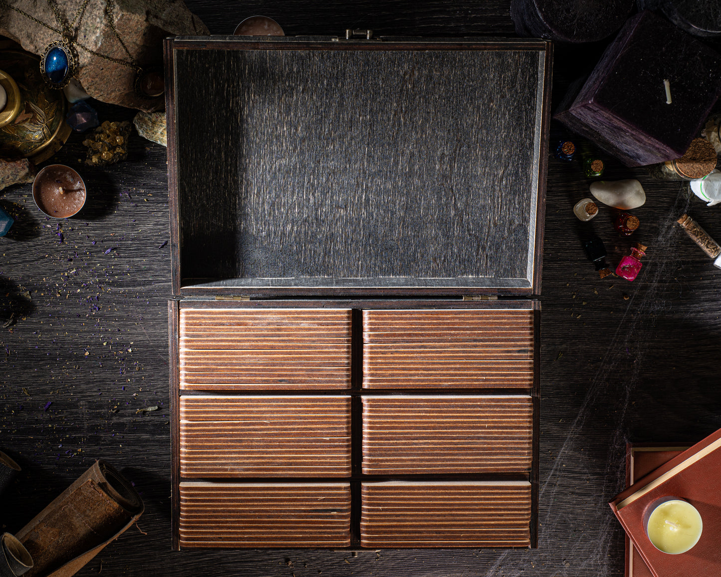 a wooden chest with six drawers, placed on a dark wooden surface. The chest is open, revealing its interior. There are also various objects scattered around the chest, including a candle, a book, and some small items.