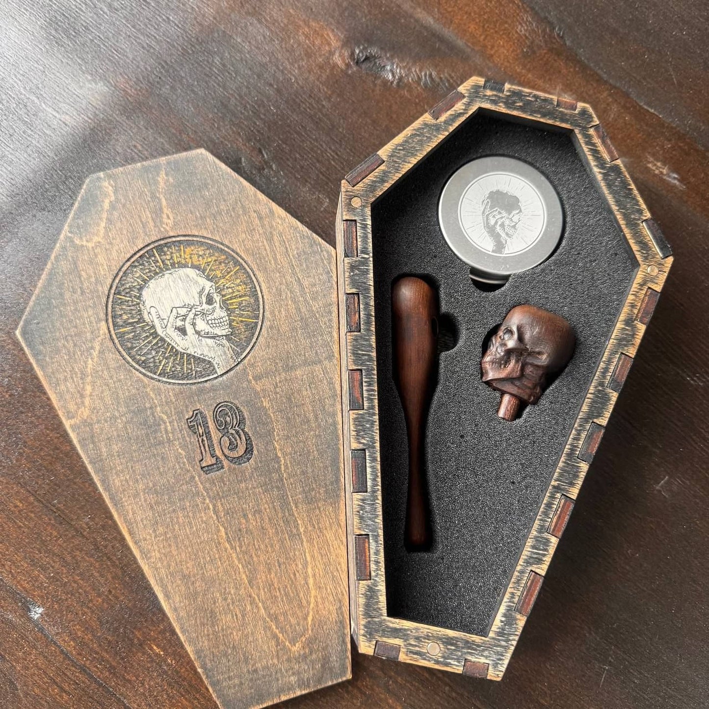 a wooden box with a skull design, containing a wooden bat and a skull-shaped object, possibly a wax seal or wax-coated object.