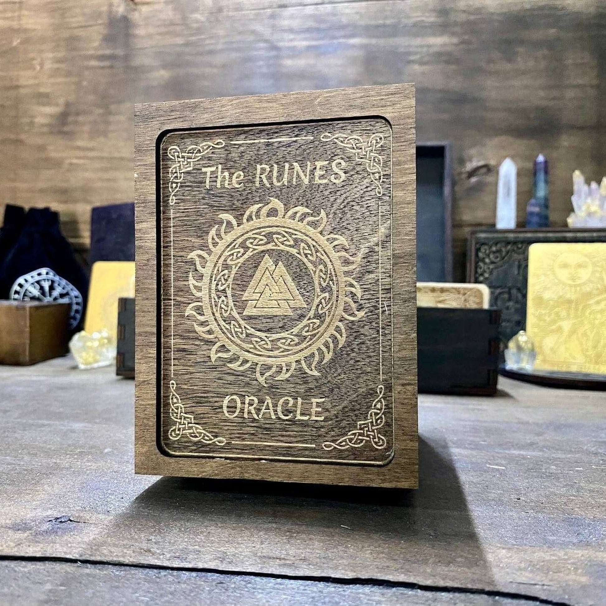 A wooden box with the text "The RUNES Oracle" engraved on it, sitting on a wooden surface.