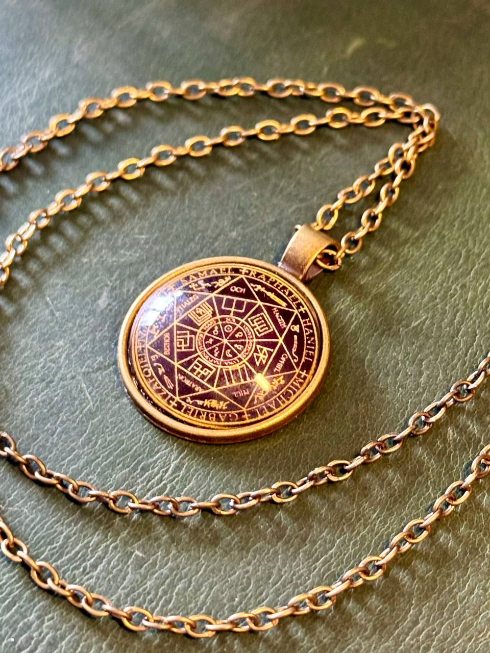 A gold-colored pendant necklace with a circular medallion featuring an intricate design, resting on a green surface.