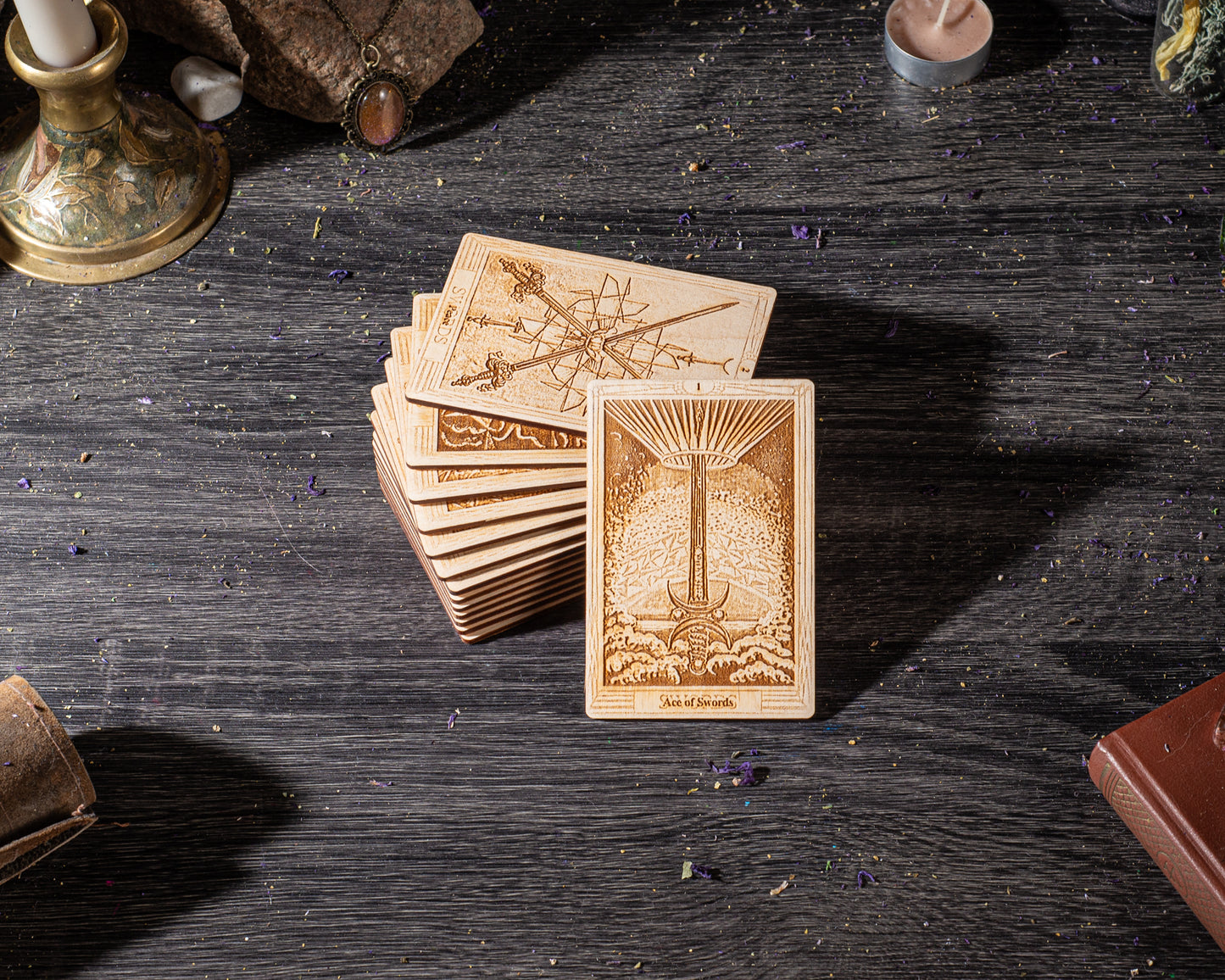 A stack of wooden tarot cards is displayed on a dark wooden surface, with a candle and other objects in the background.