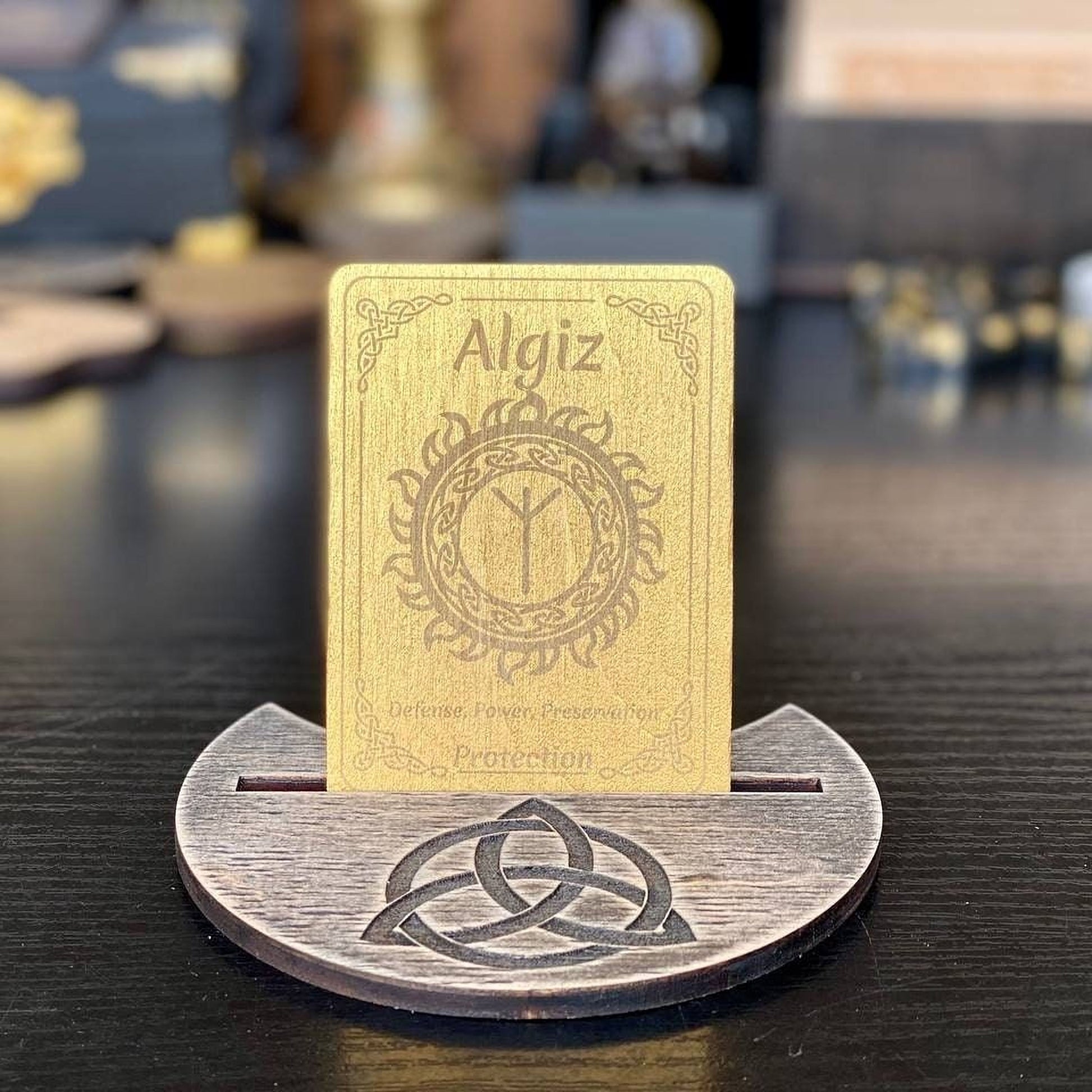 A wooden stand displaying a gold-colored card with the name Algiz and a Celtic knot design.