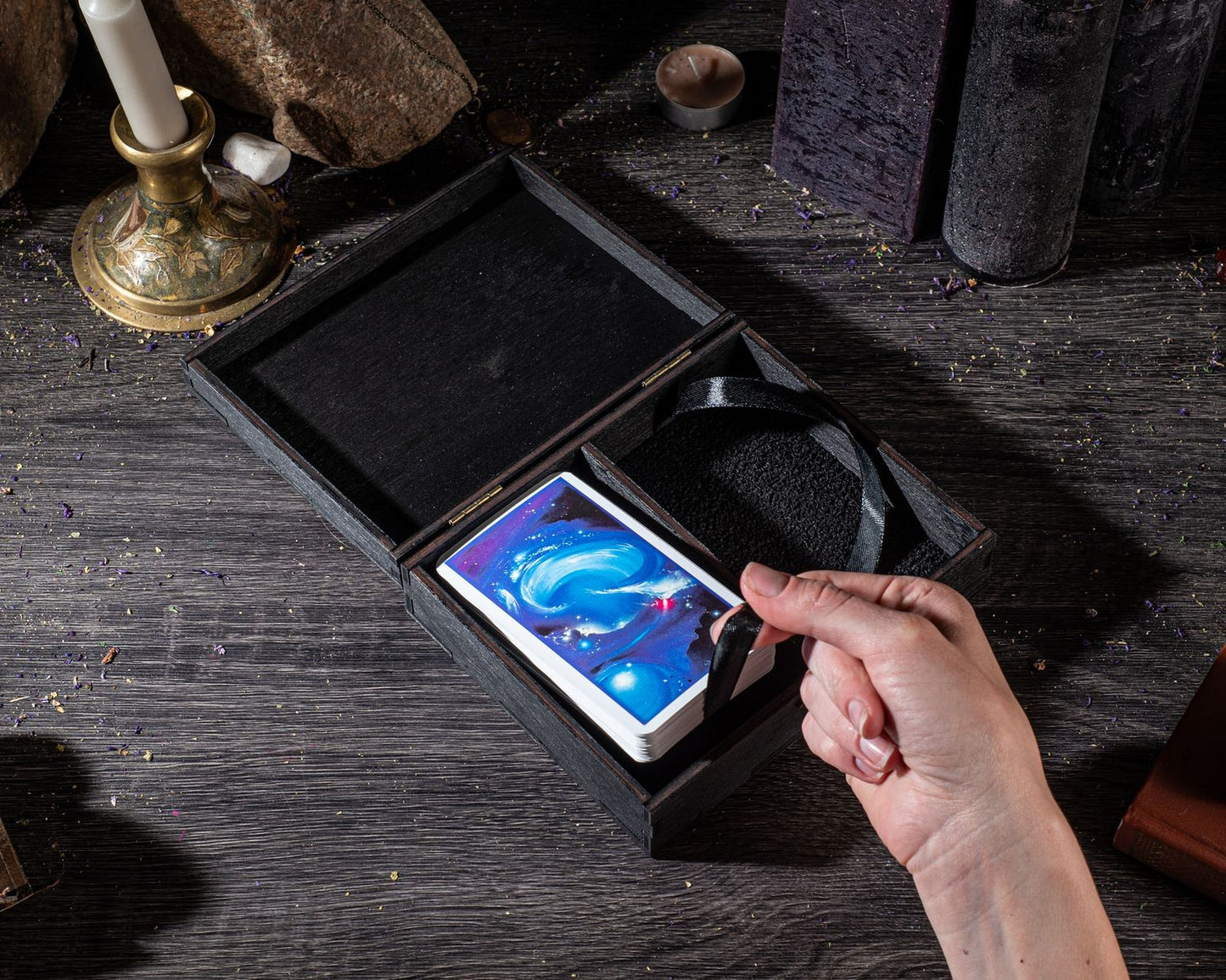 A hand is holding a deck of cards from a wooden box, which is placed on a wooden surface.