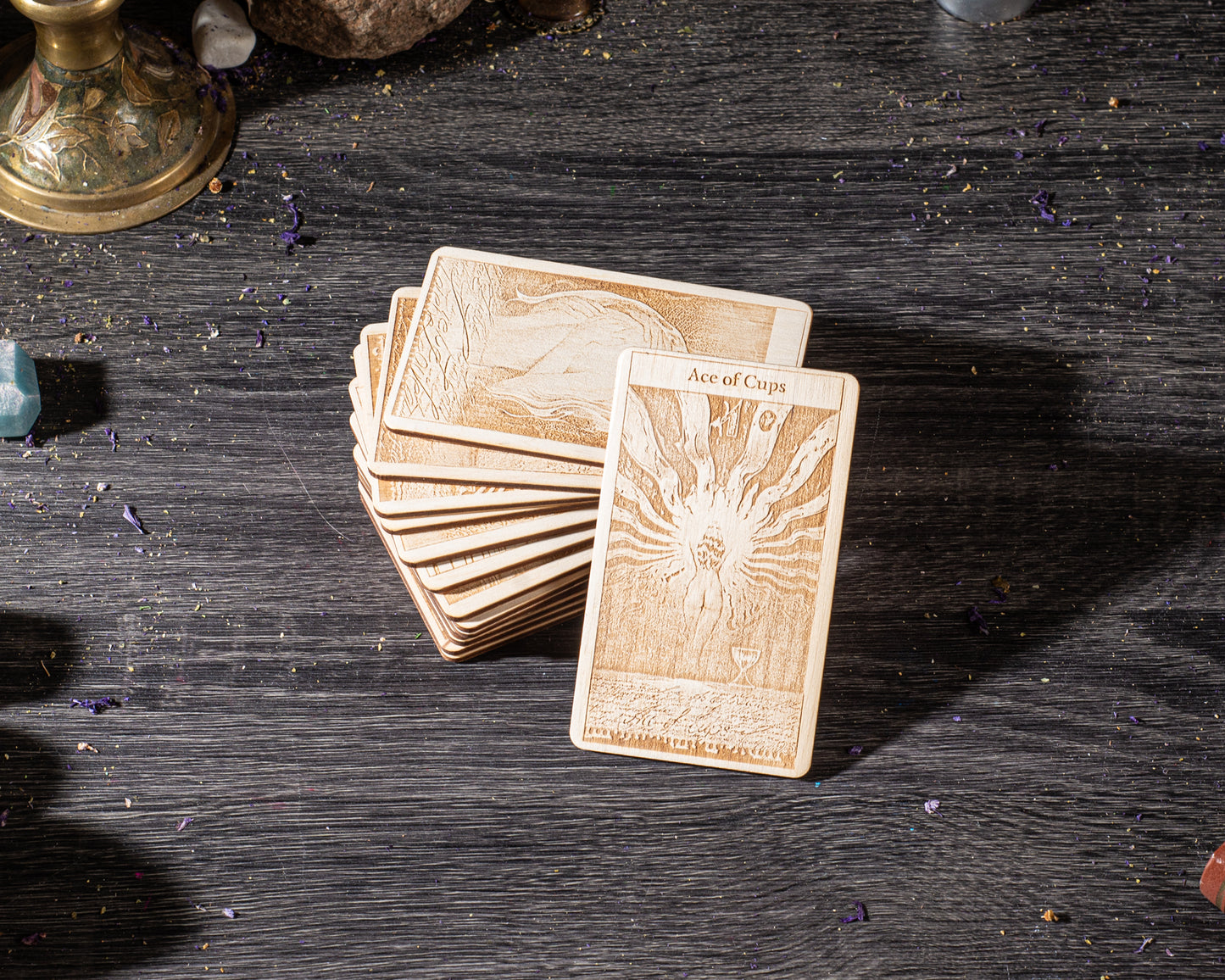 A stack of wooden tarot cards is displayed on a dark wooden surface, with scattered purple and blue objects around them.