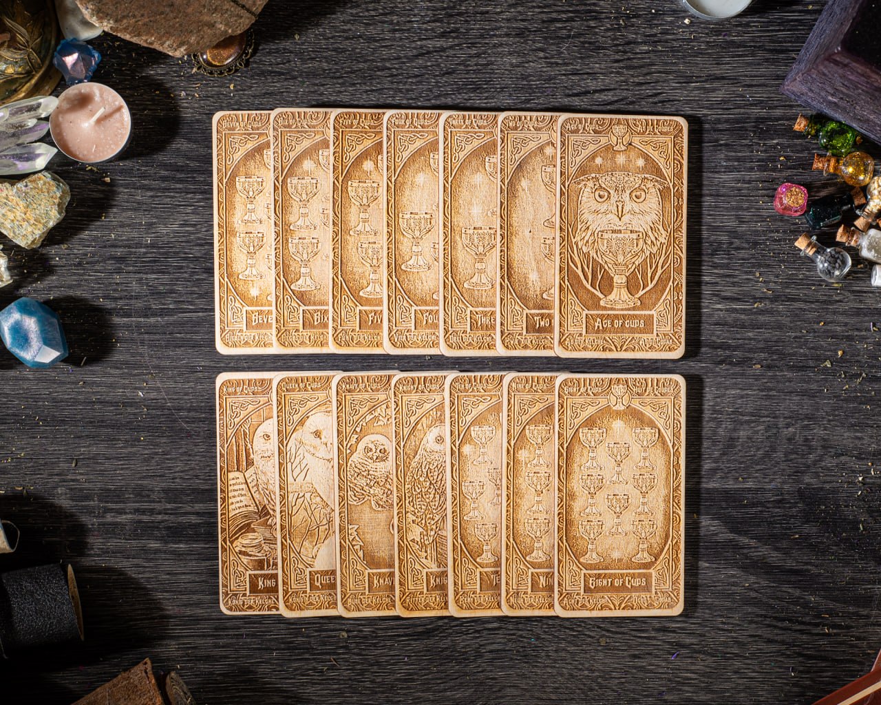 A collection of wooden tarot cards arranged on a dark wooden surface, with various objects such as gemstones and candles scattered around them.