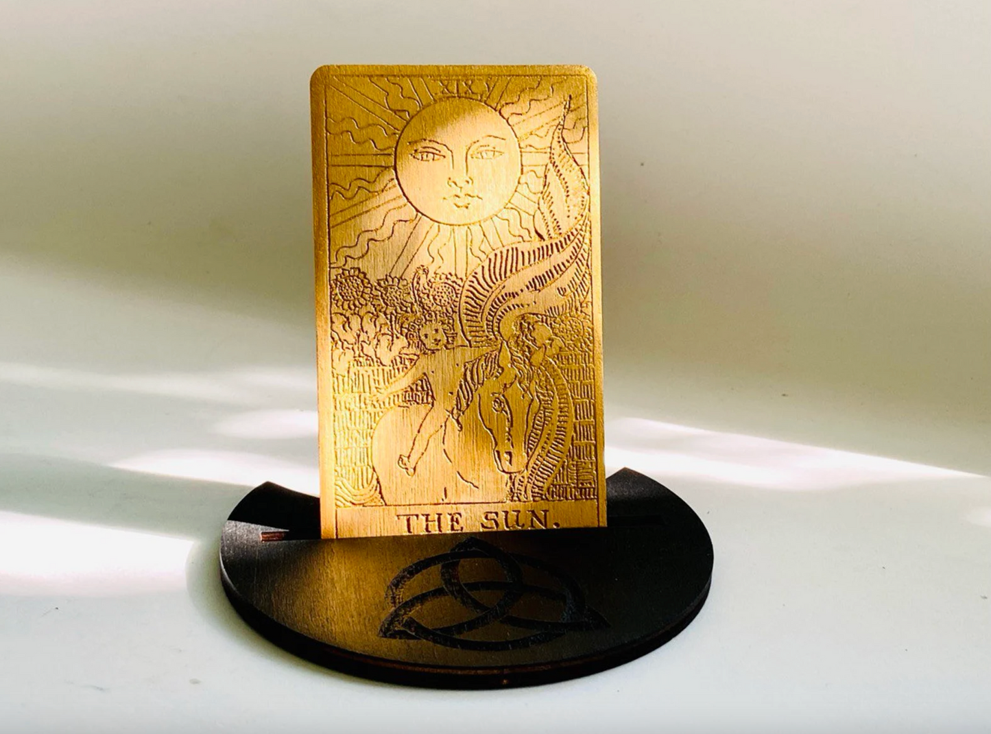 a golden tarot card standing upright on a black stand, with the word "THE SUN" written on it.