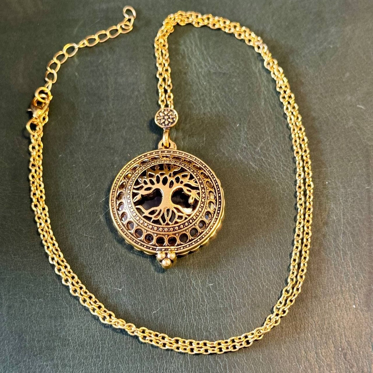 A gold-colored necklace with a circular pendant featuring a tree design.