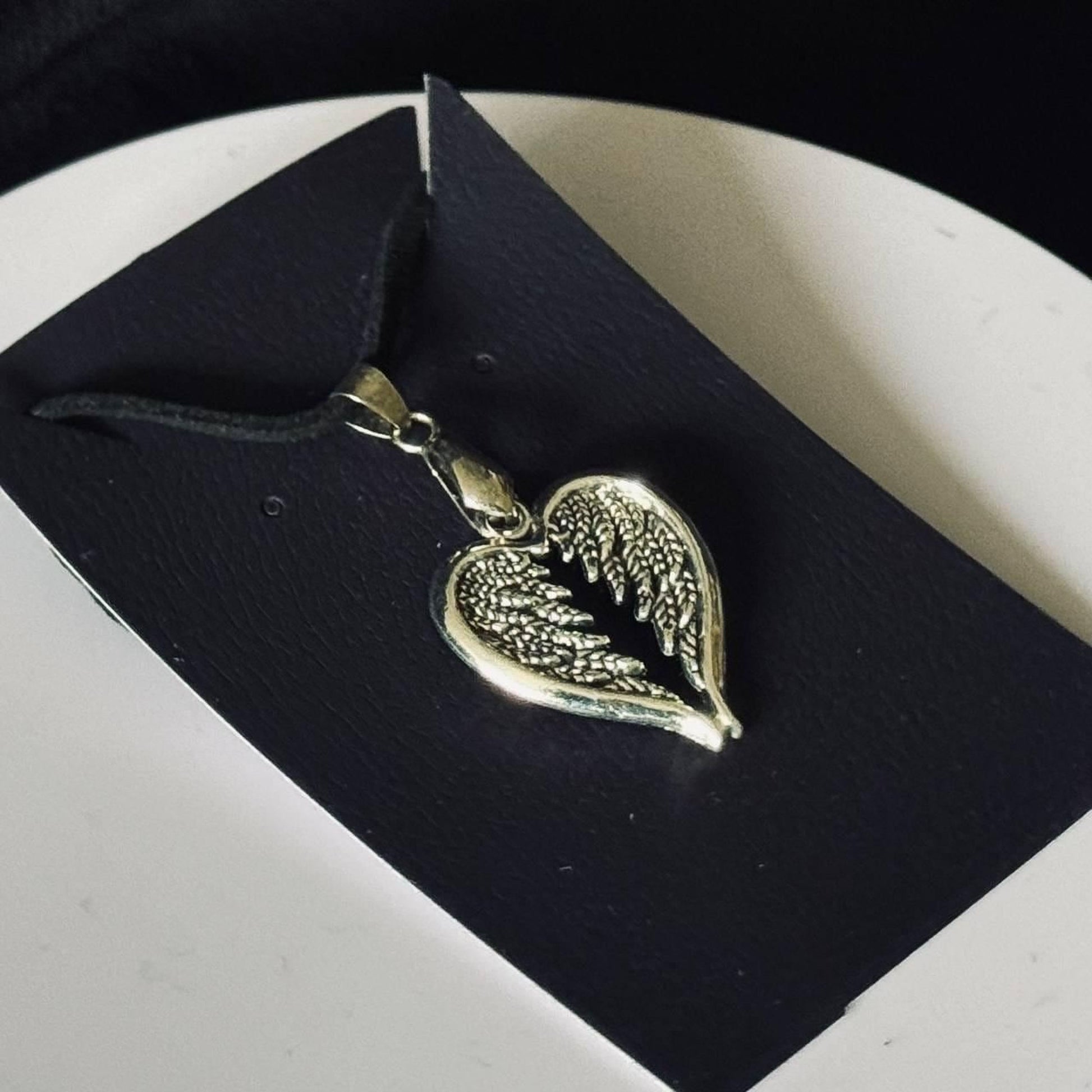 A silver heart-shaped pendant with feather-like details is displayed on a black background.