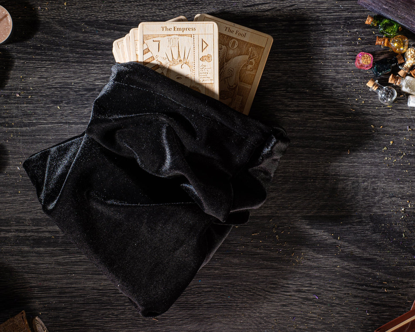 A black velvet pouch containing several tarot cards is placed on a dark wooden surface, with scattered objects around it.