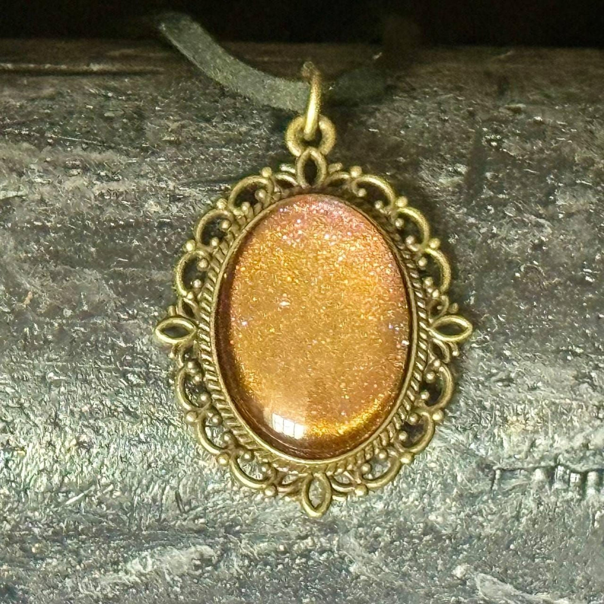 A decorative pendant with a gold-colored stone or gemstone, hanging from a chain or cord.