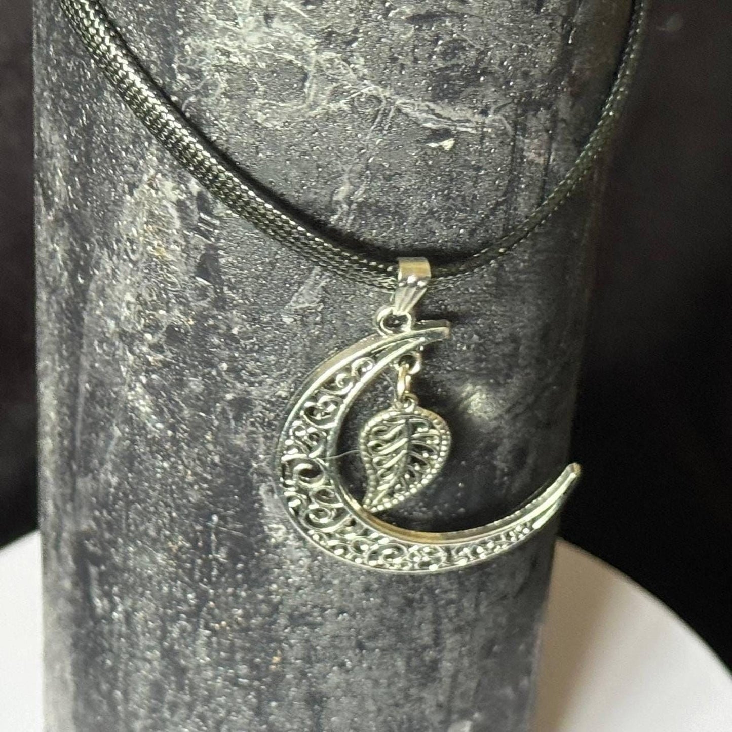 A silver pendant necklace with a crescent moon and leaf design.