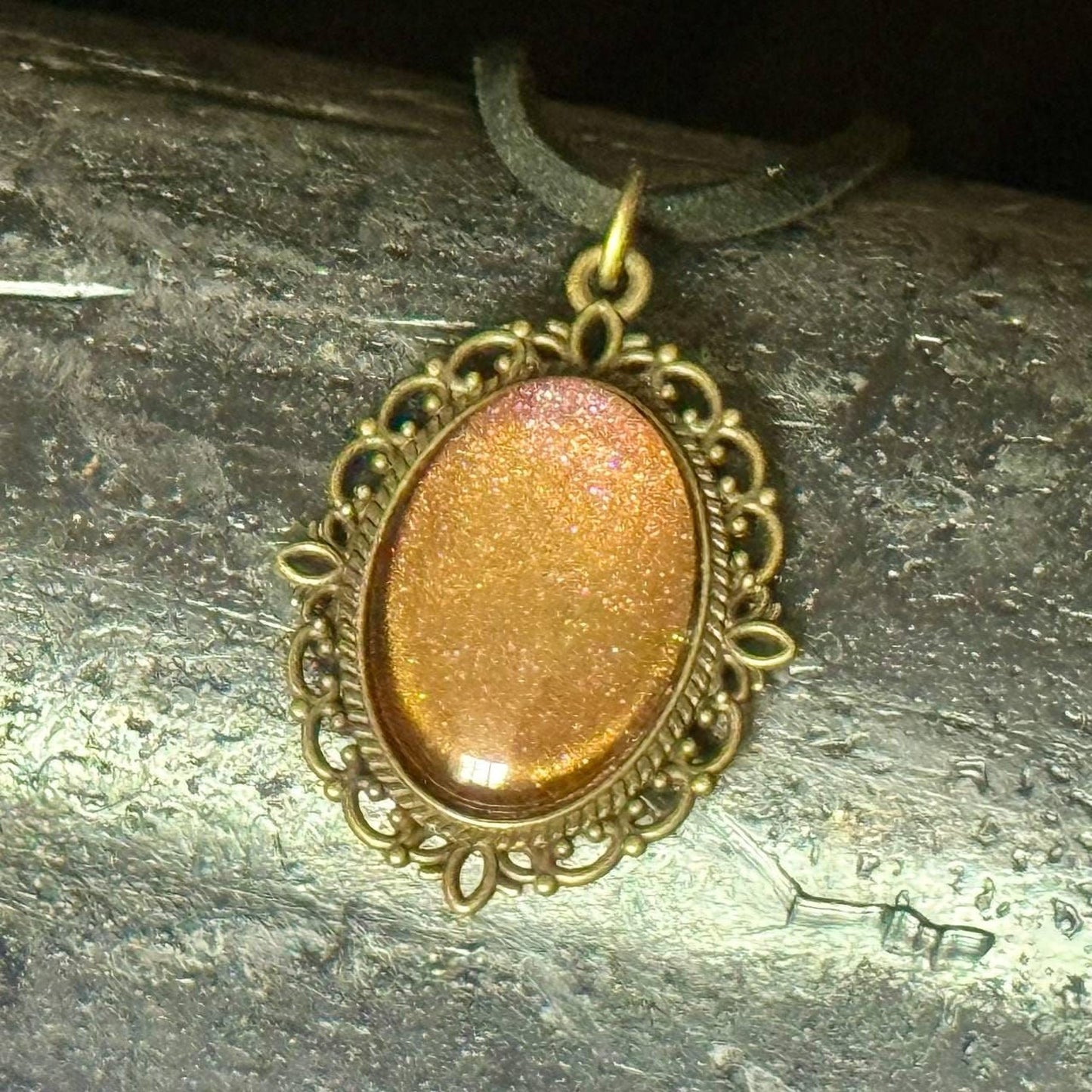 A decorative pendant with a gold-colored oval-shaped stone or gemstone, hanging from a chain or cord.