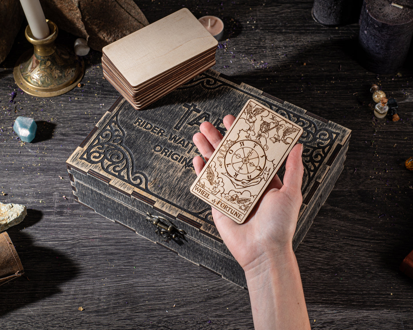 A hand holding a wooden tarot card with intricate designs, placed on a wooden box with a similar design.