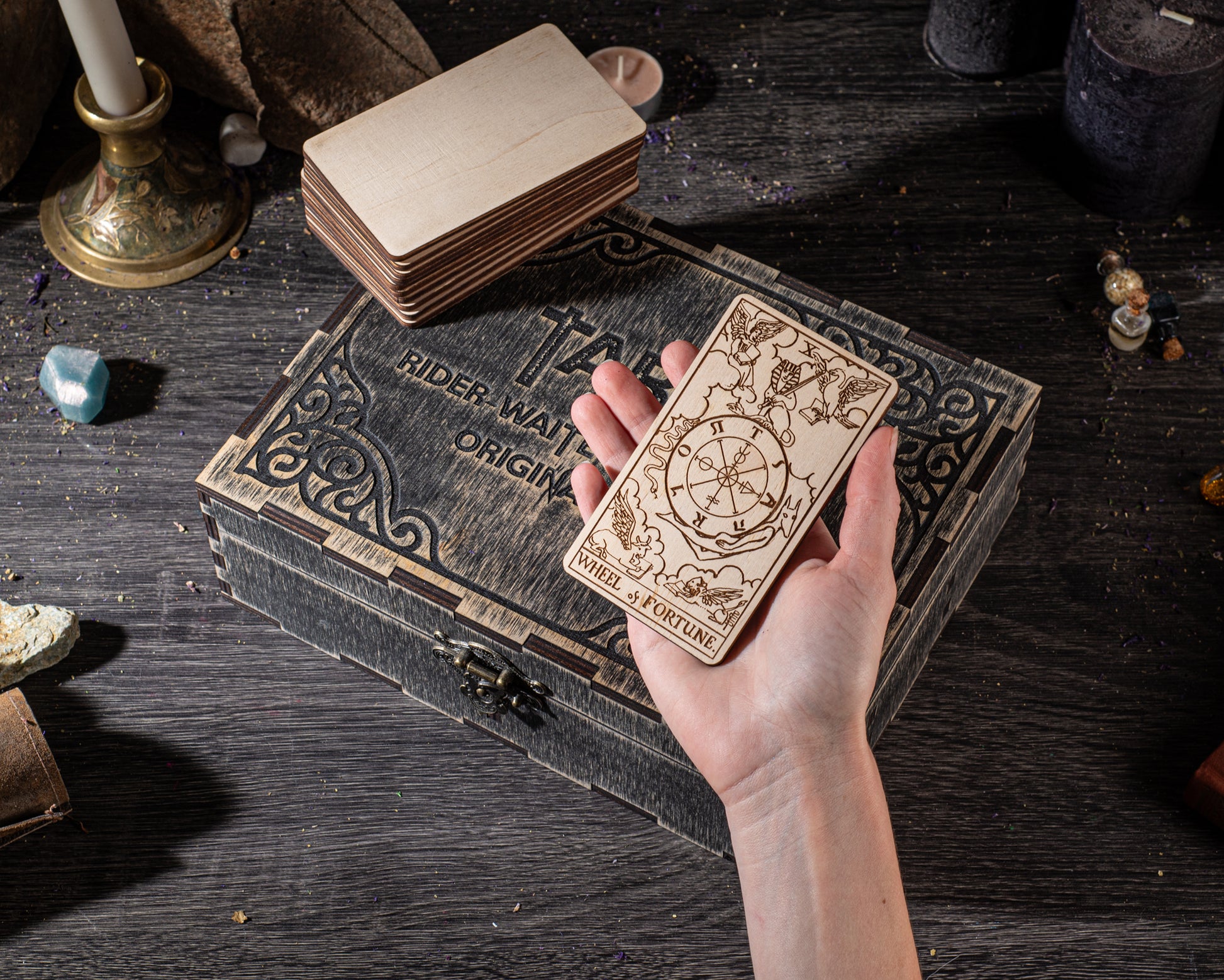 A hand holding a wooden tarot card with intricate designs, placed on a wooden box with a similar design.
